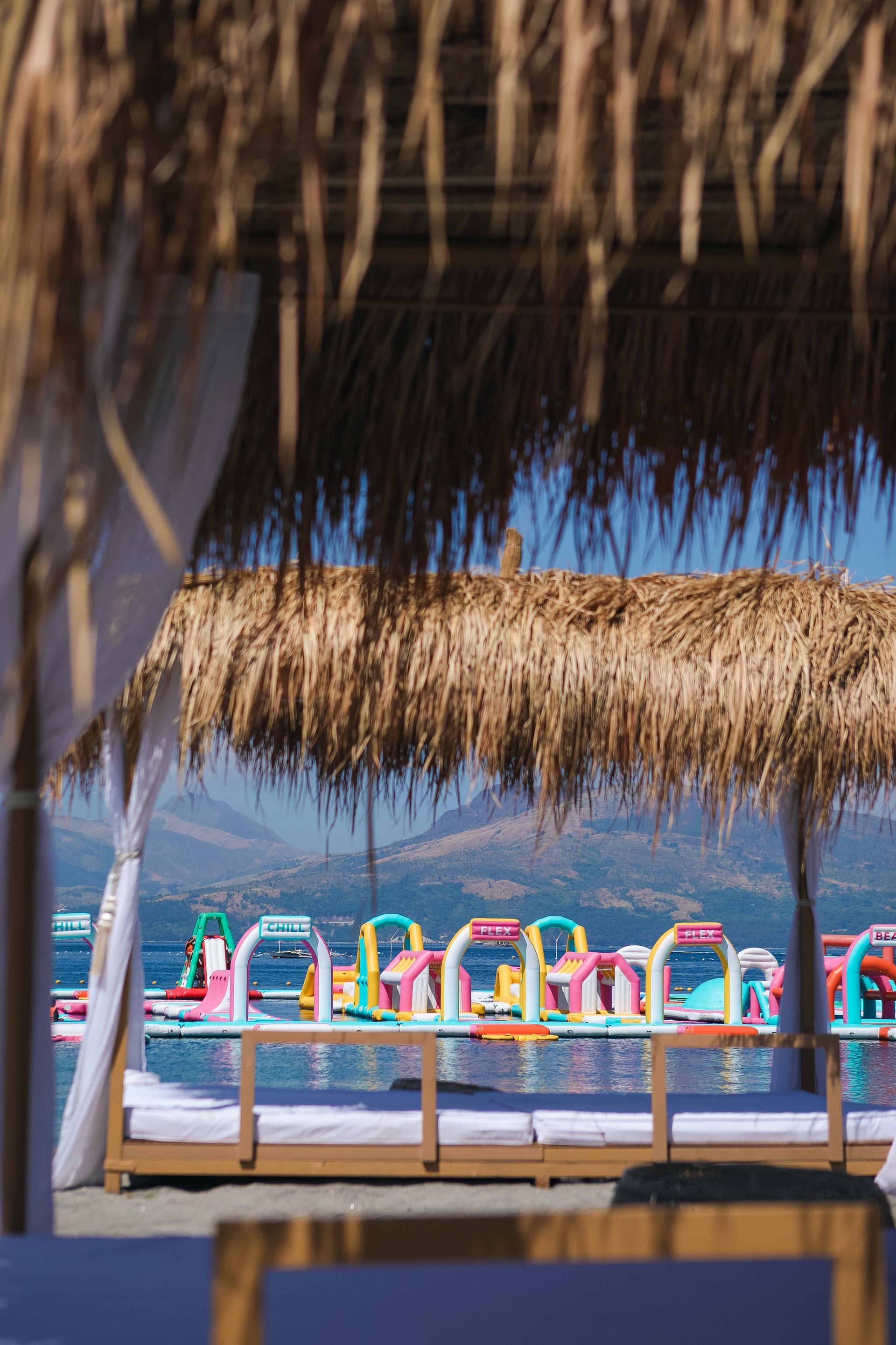 Colorful lounge chairs under thatched palapas on a sunny beach with blue sea in the background