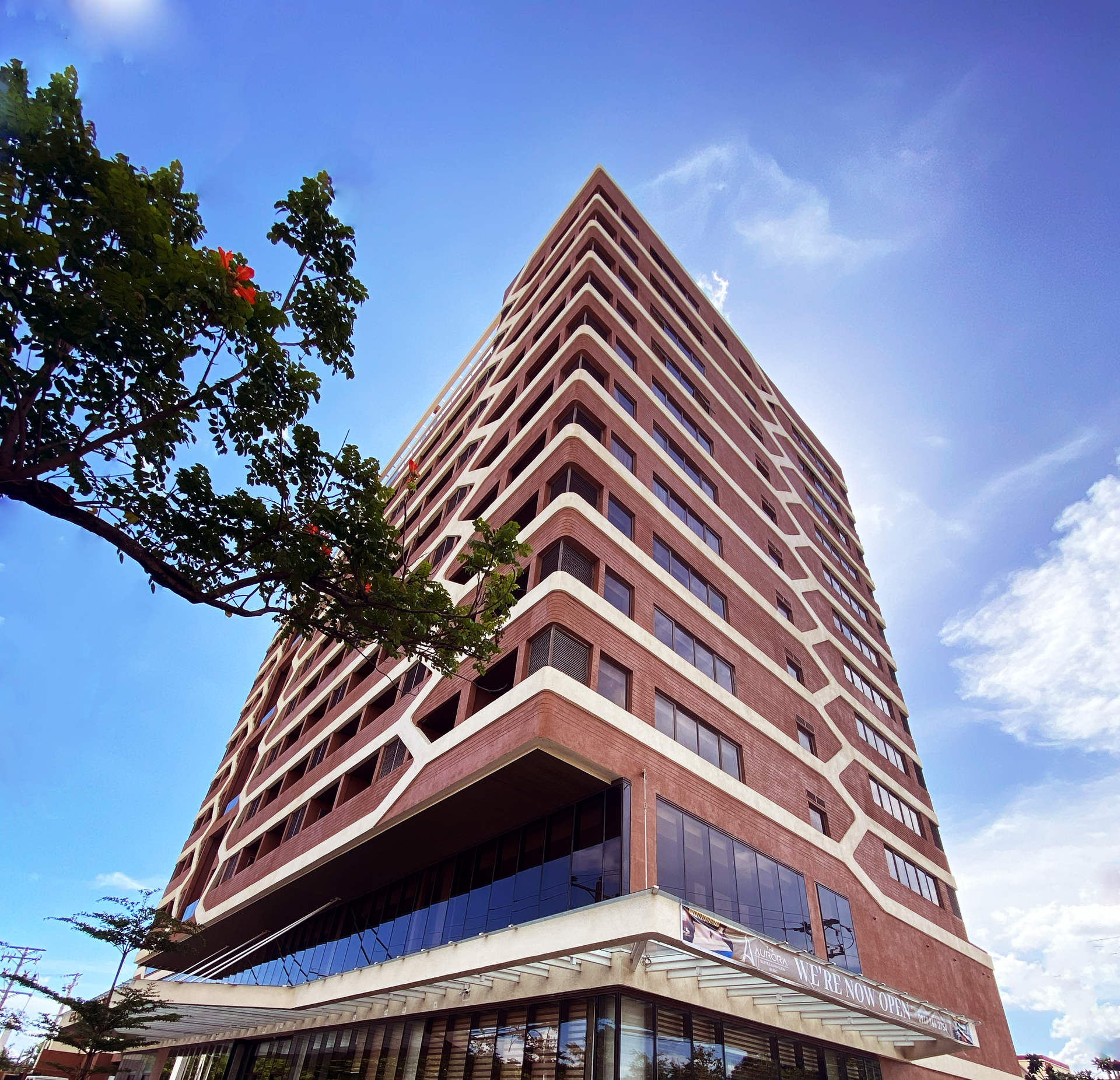 Low-angle view of a tall red-brick high-rise against a blue sky with tree branches in the foreground