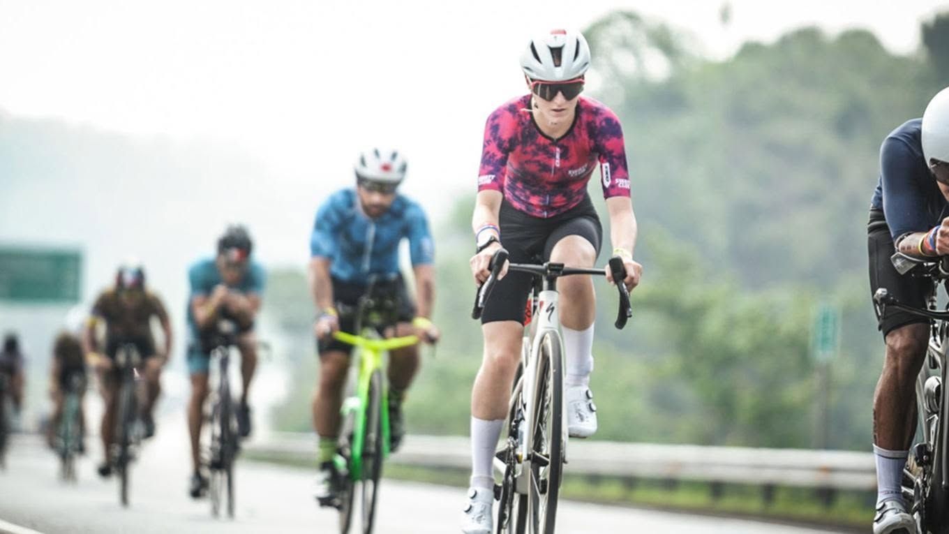Cyclists racing on a wet road, with a rider in a pink jersey leading the group.