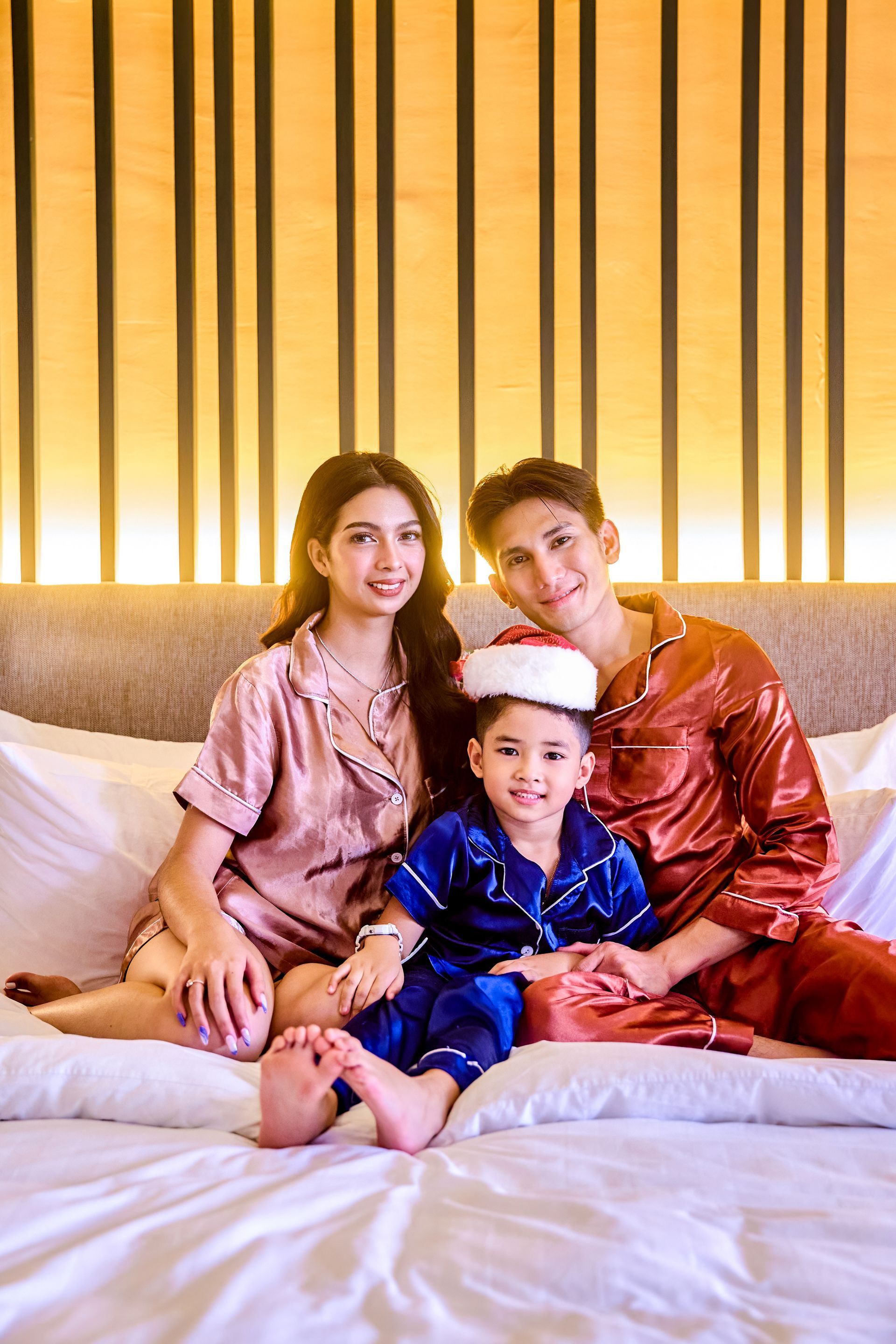 Family in satin pajamas with Santa hat on bed at The Aurora Subic Hotel