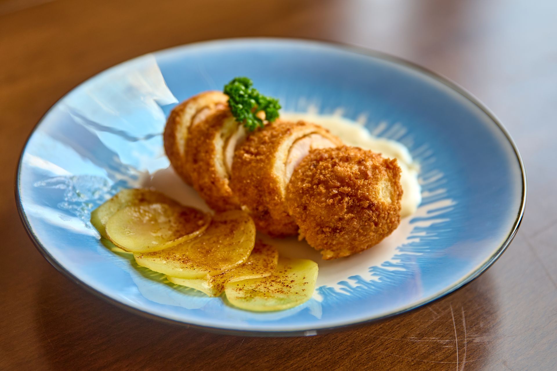 Crispy breaded chicken Kiev with pickle slices on blue plate