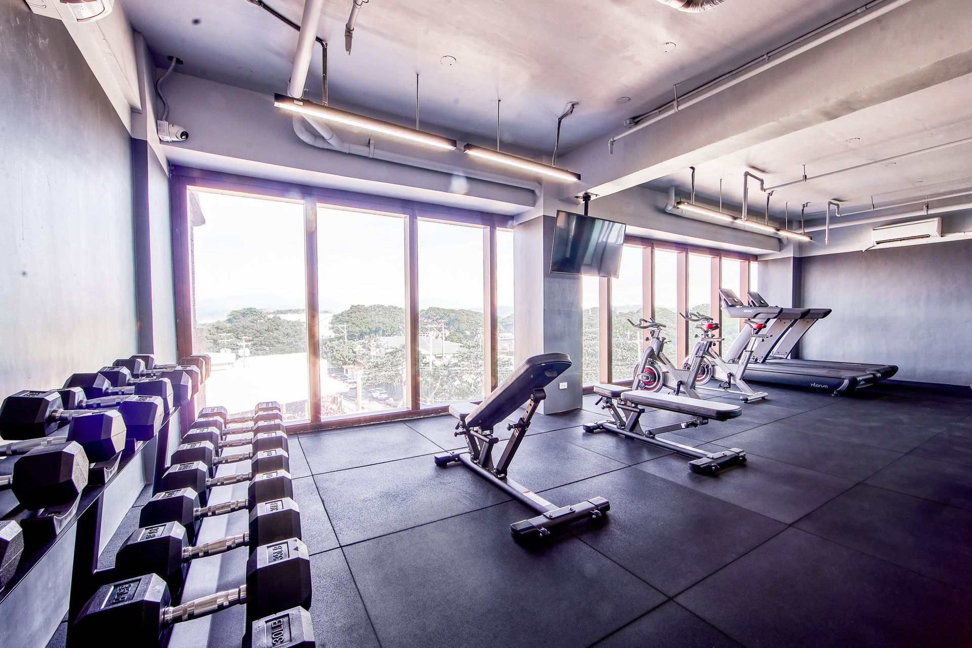 Gym with weights, benches, and cardio equipment near large windows with a view.