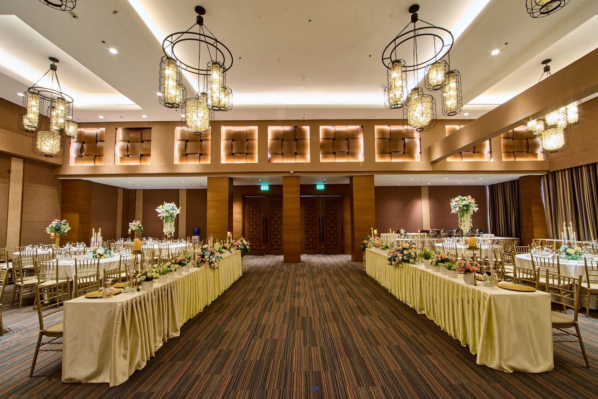 Elegant banquet hall with long decorated tables, chandeliers, and wooden double doors at the far end