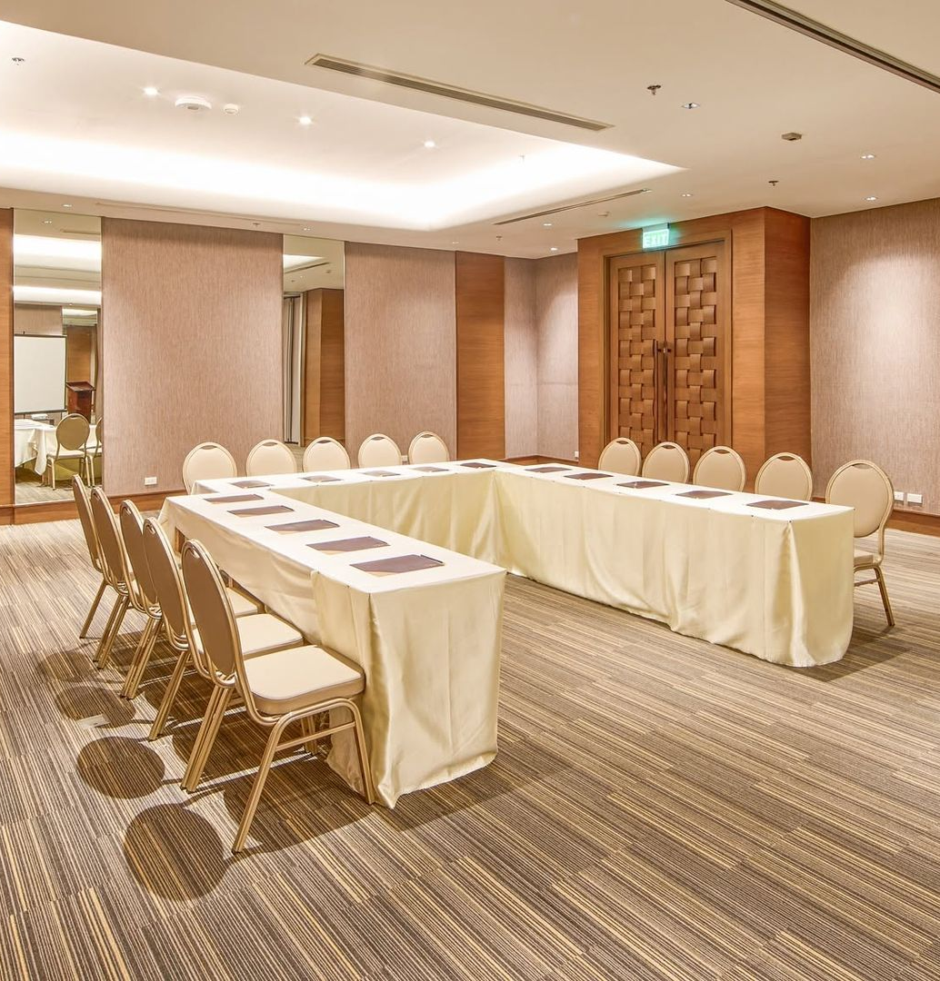 Conference room with U-shaped tables, beige chairs, and a carpeted floor in warm lighting