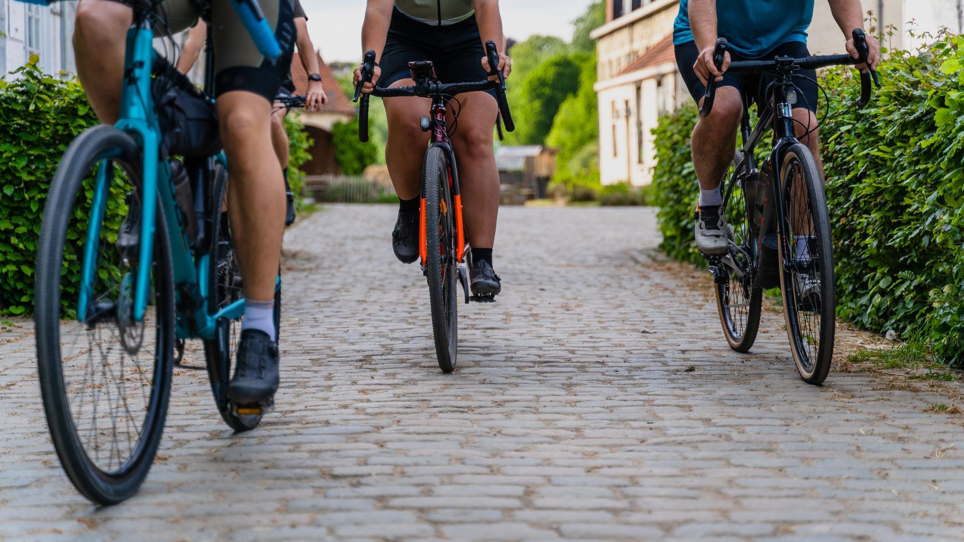 Cyclists riding on a cobblestone path, front wheels and legs visible in a outdoor neighborhood setting