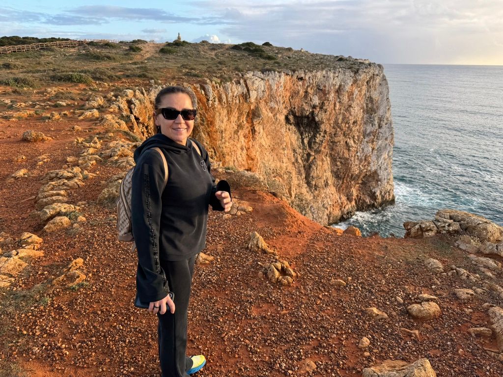 Woman standing on red cliffside overlooking ocean.