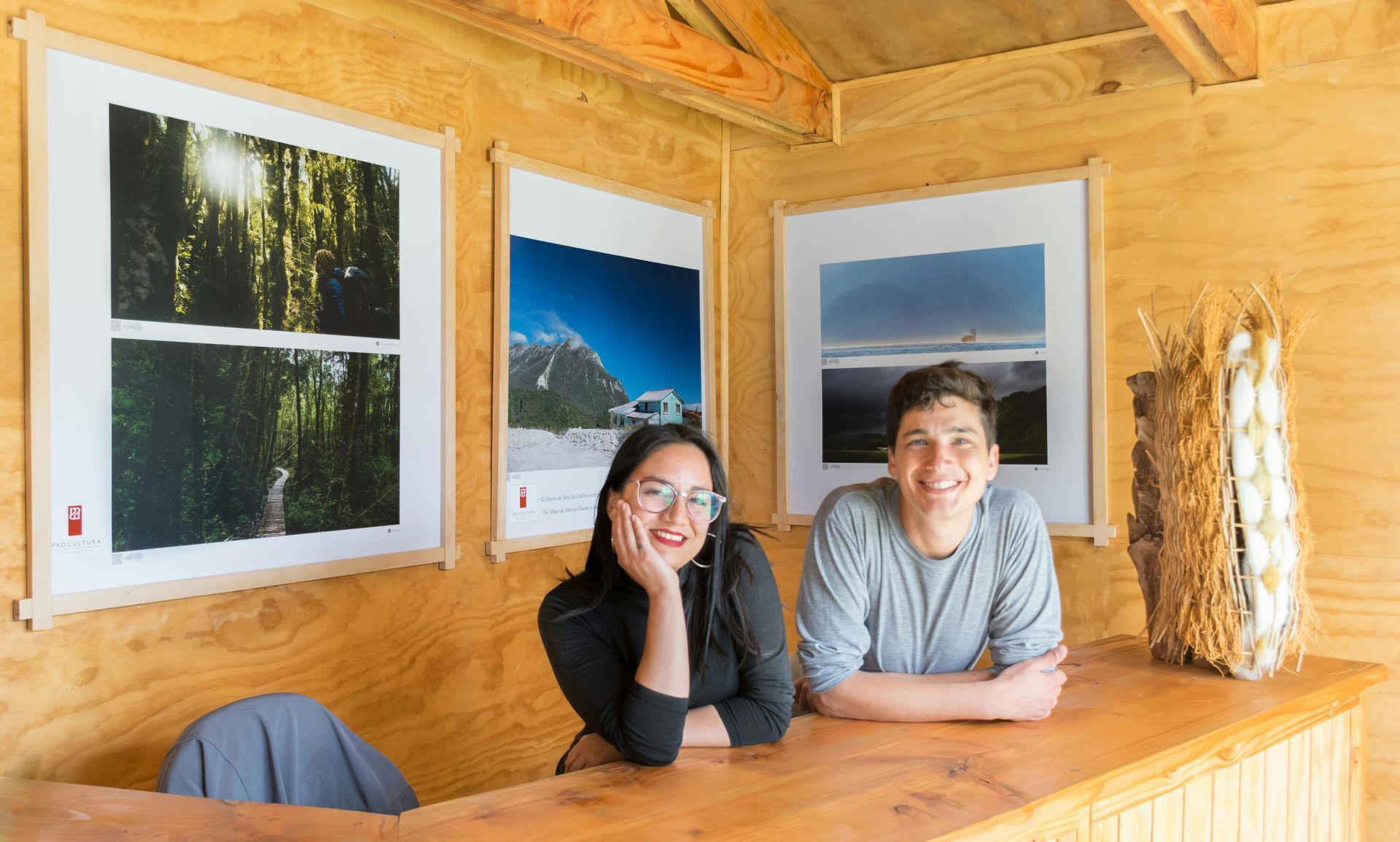 Dos personas sonriendo ante un mostrador de madera, con fotografías de la naturaleza enmarcadas detrás de ellas.