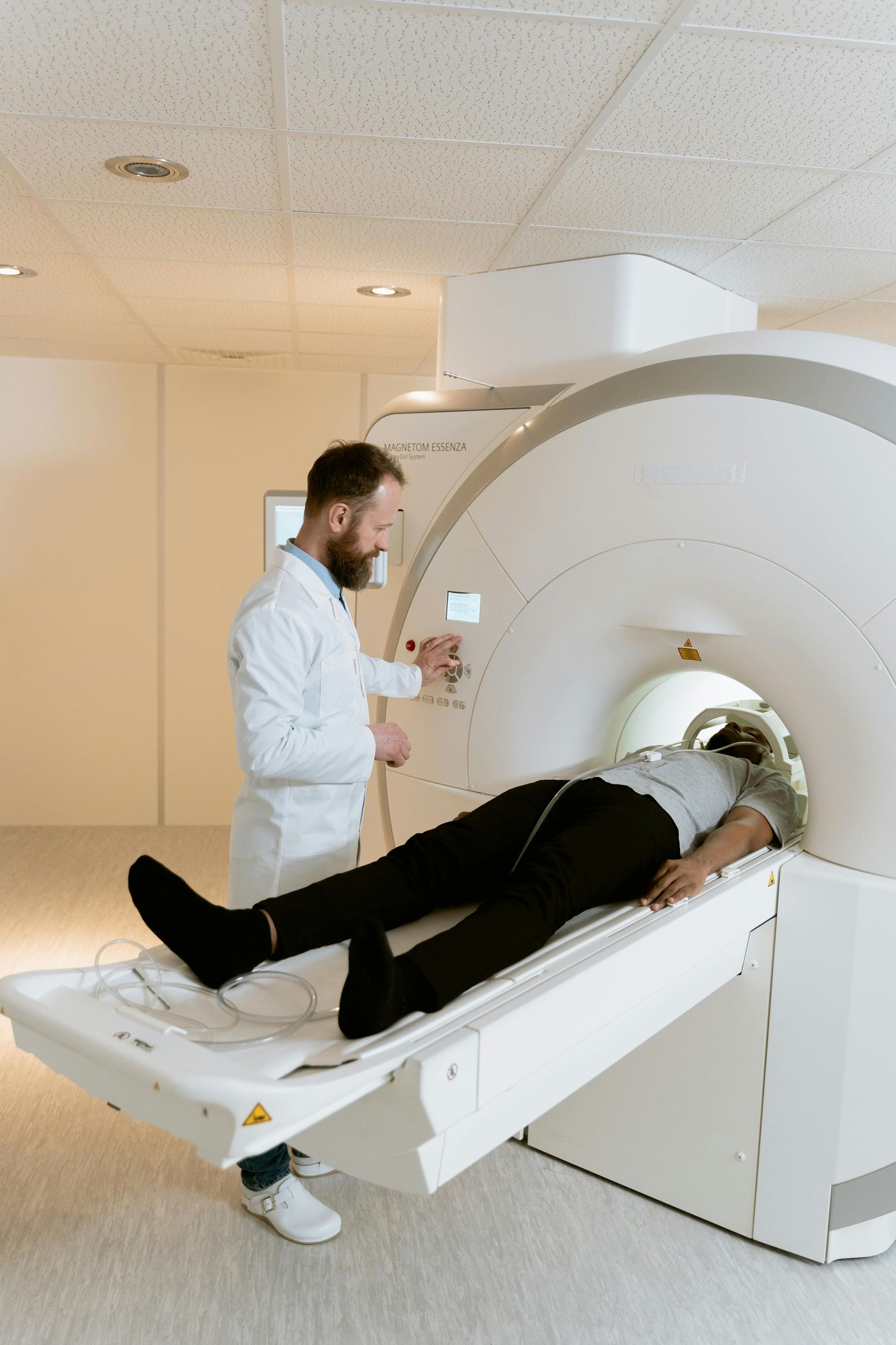 Persona en una máquina de resonancia magnética, médico ajustando controles. Sala médica blanca.