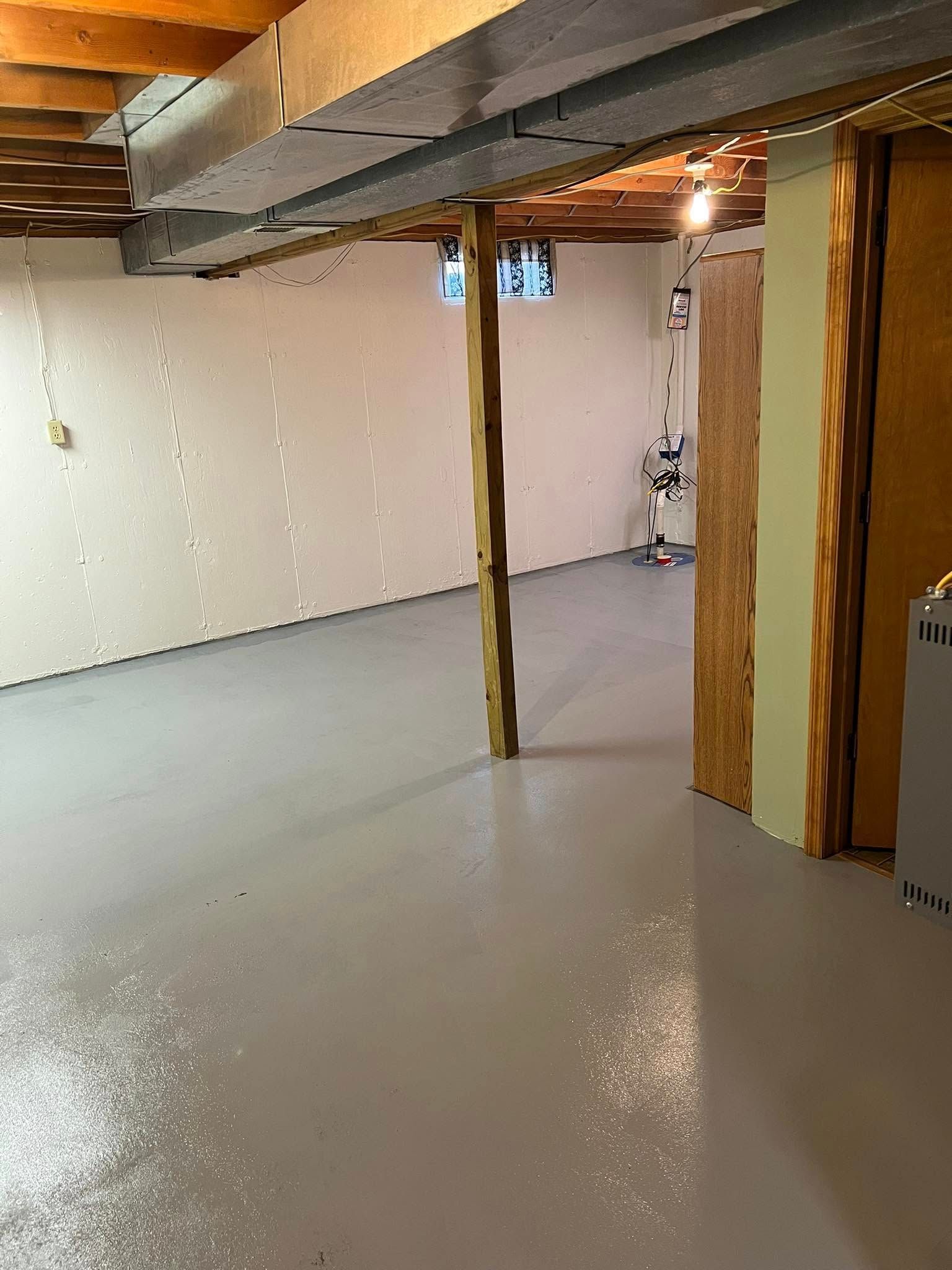 Empty basement room with white floor, exposed beams, and unfinished walls