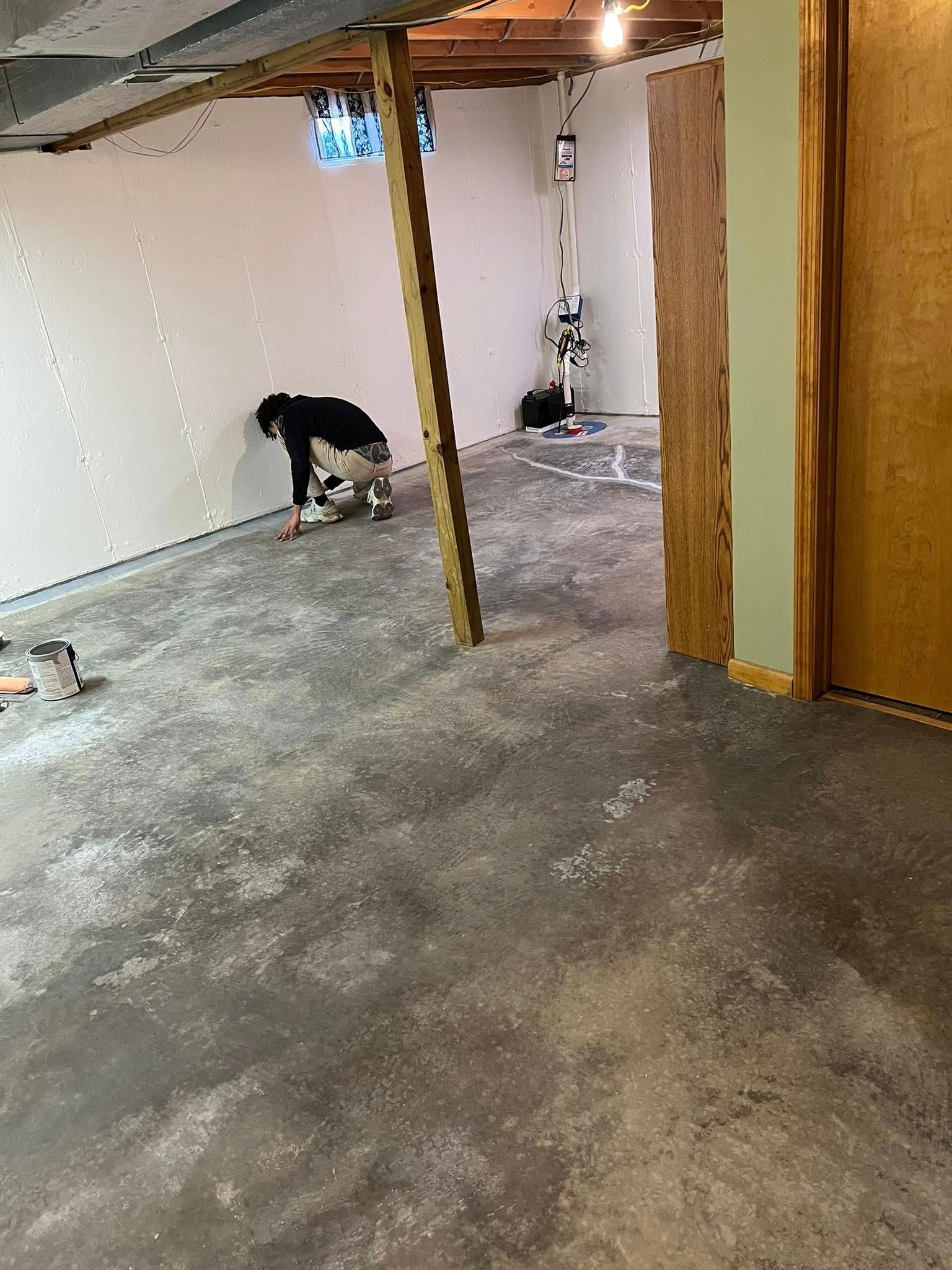 Partially finished basement with concrete floor, exposed beams, and a person crouching near the wall