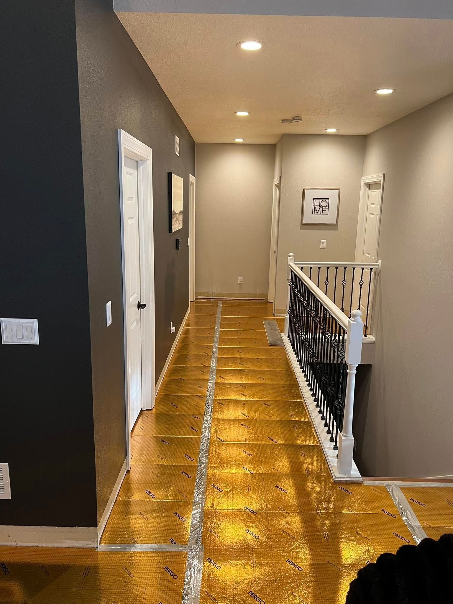 Bright hallway with glossy wood floor, recessed lights, and white railing along a staircase landing.