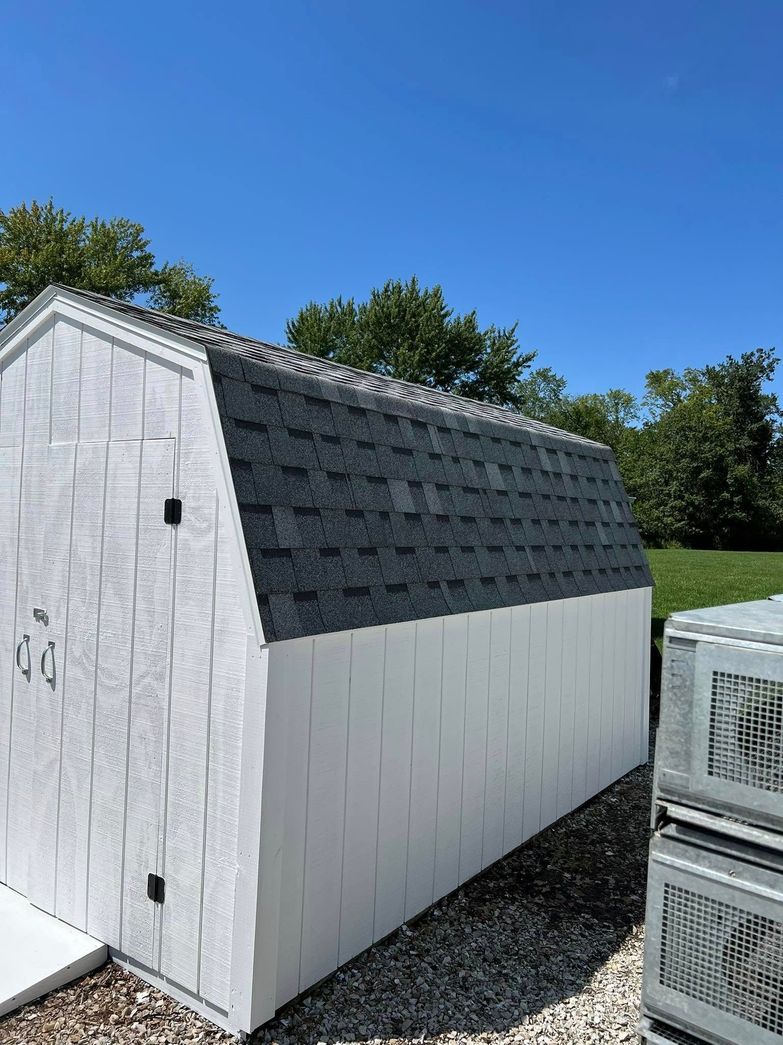 White shed with gray roof panels beside a grassy yard under a blue sky