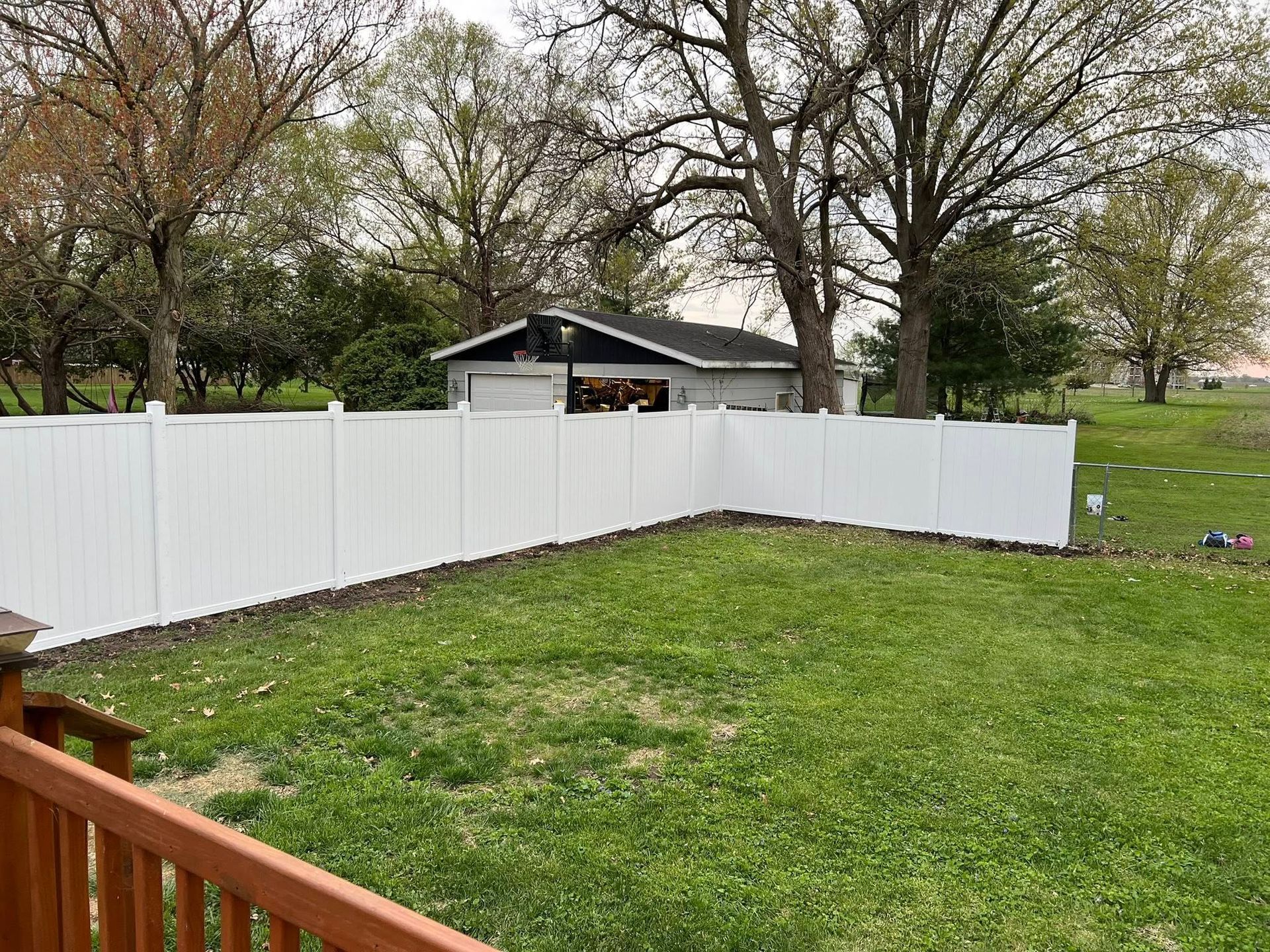 Backyard with white vinyl fence, green lawn, and trees, with a small shed in the background