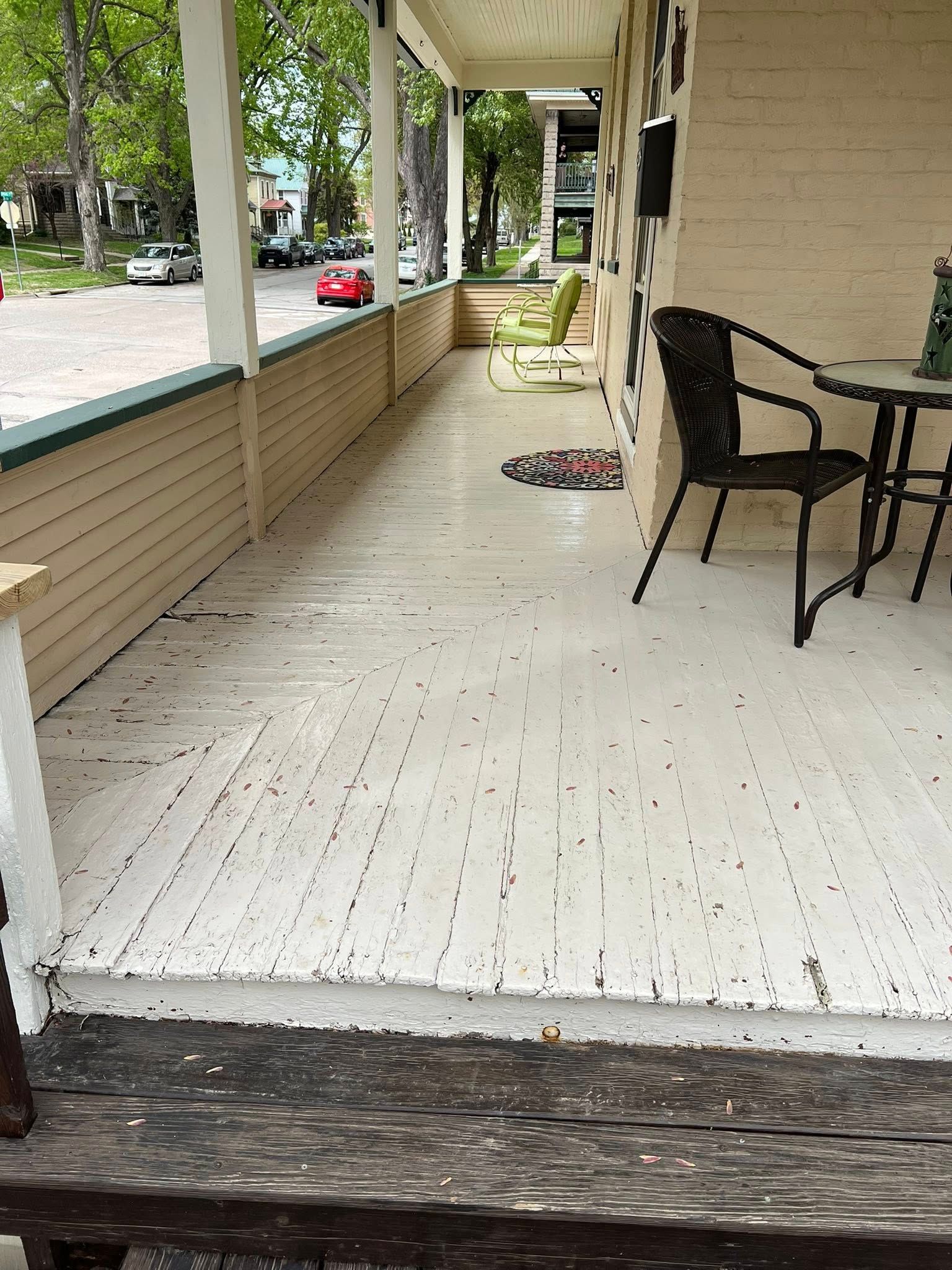 Covered porch with white floor, beige siding, black chair and table, and a view of the street.