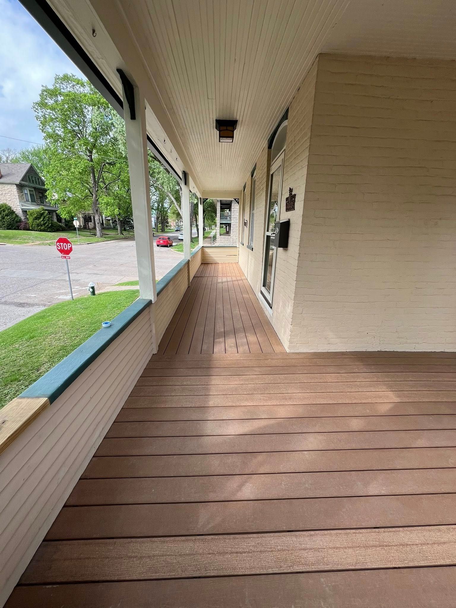 Long covered apartment walkway with white siding, brown floorboards, and green lawn along the side
