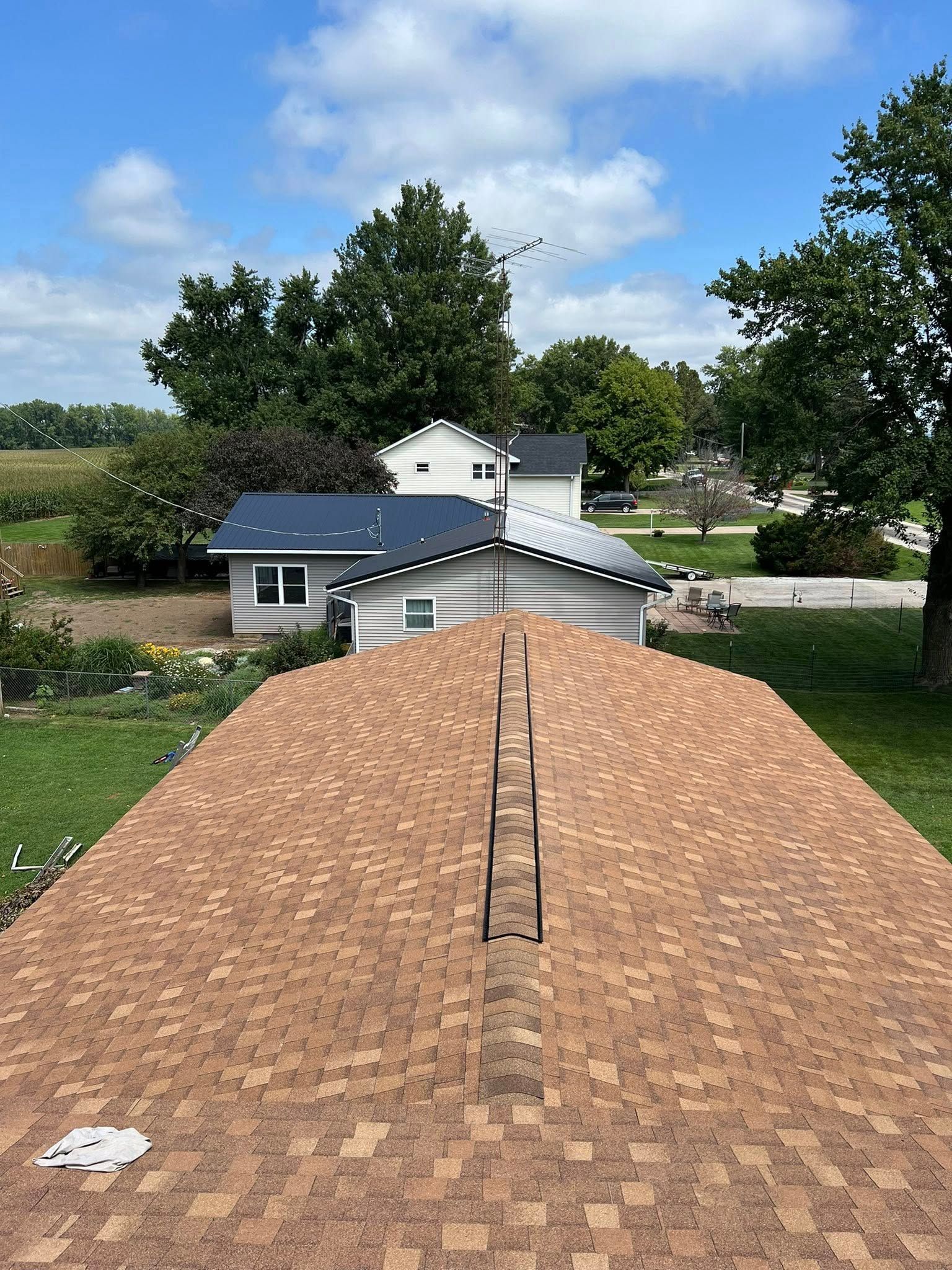 Shingled rooftop with a ridge vent, overlooking trees and houses under a blue sky