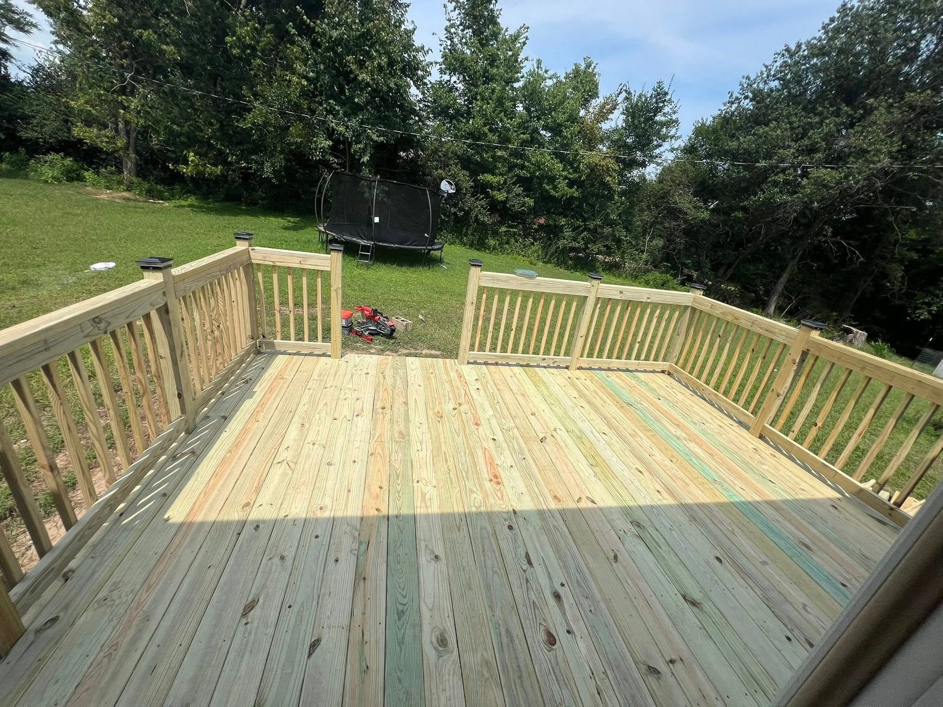 Freshly built light wood deck with railings overlooking a grassy backyard and trees