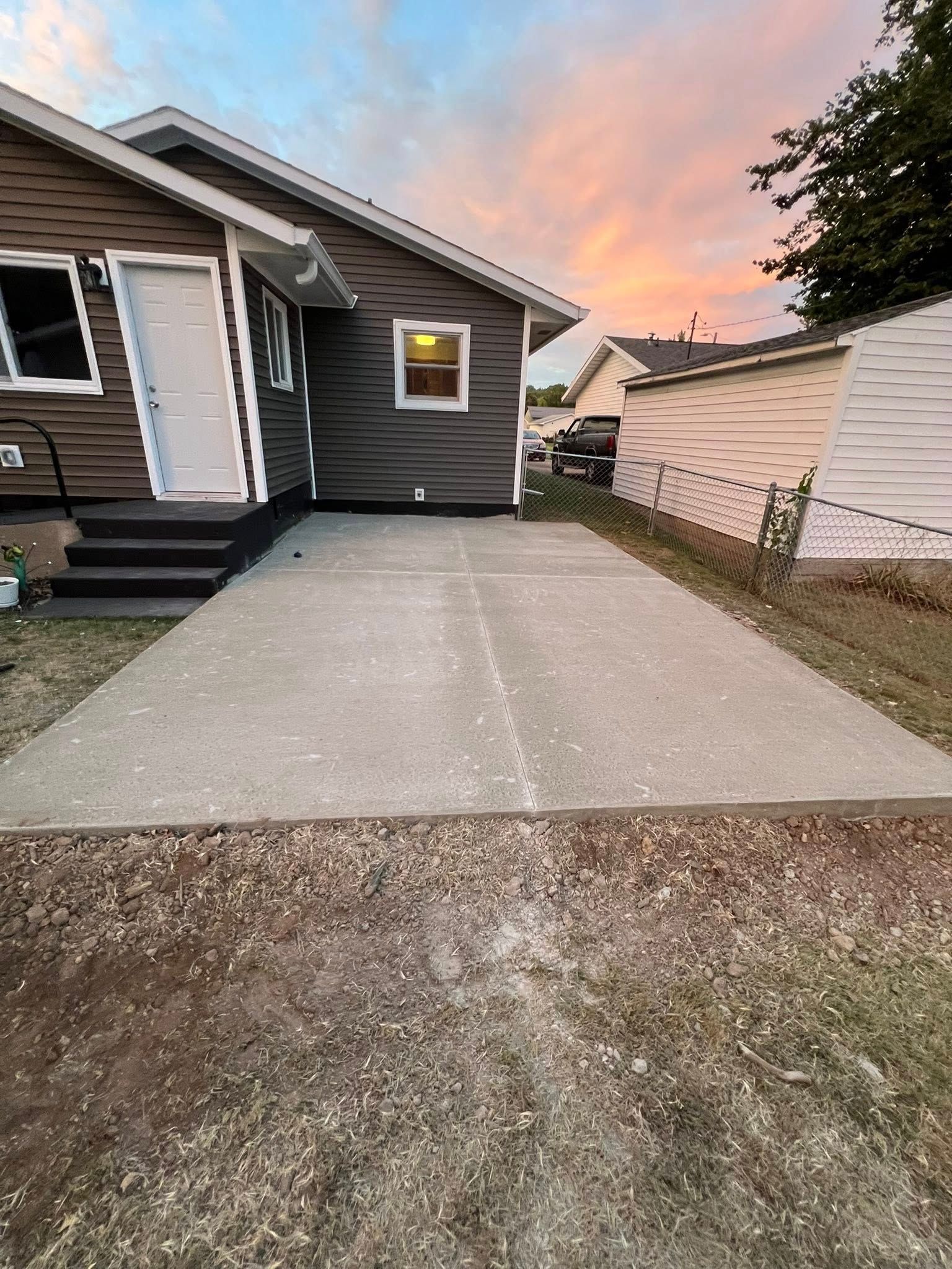 Driveway beside a gray house and white garage at sunset, with pink clouds overhead.