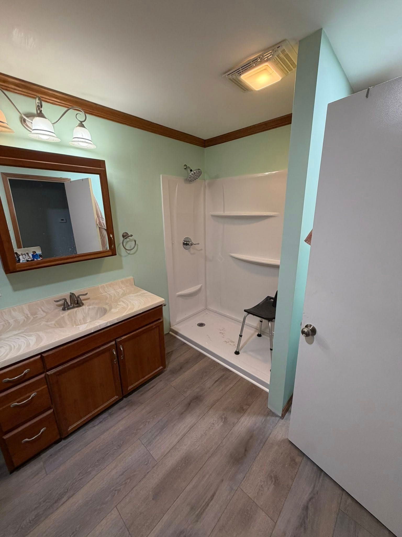 Bathroom with vanity, mirror, shower stall, and open door, featuring mint walls and wood trim