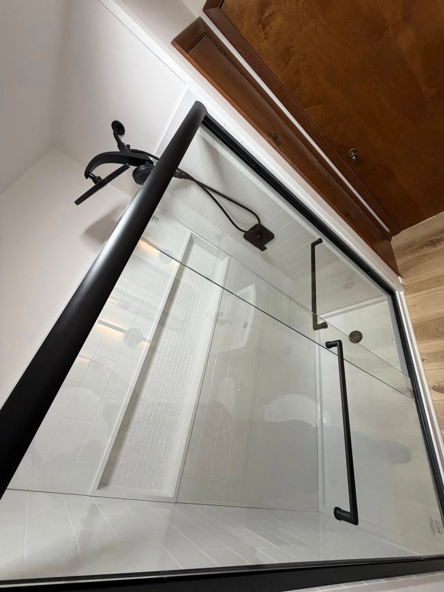 Glass shower enclosure with black frame and handle under a wooden ceiling panel