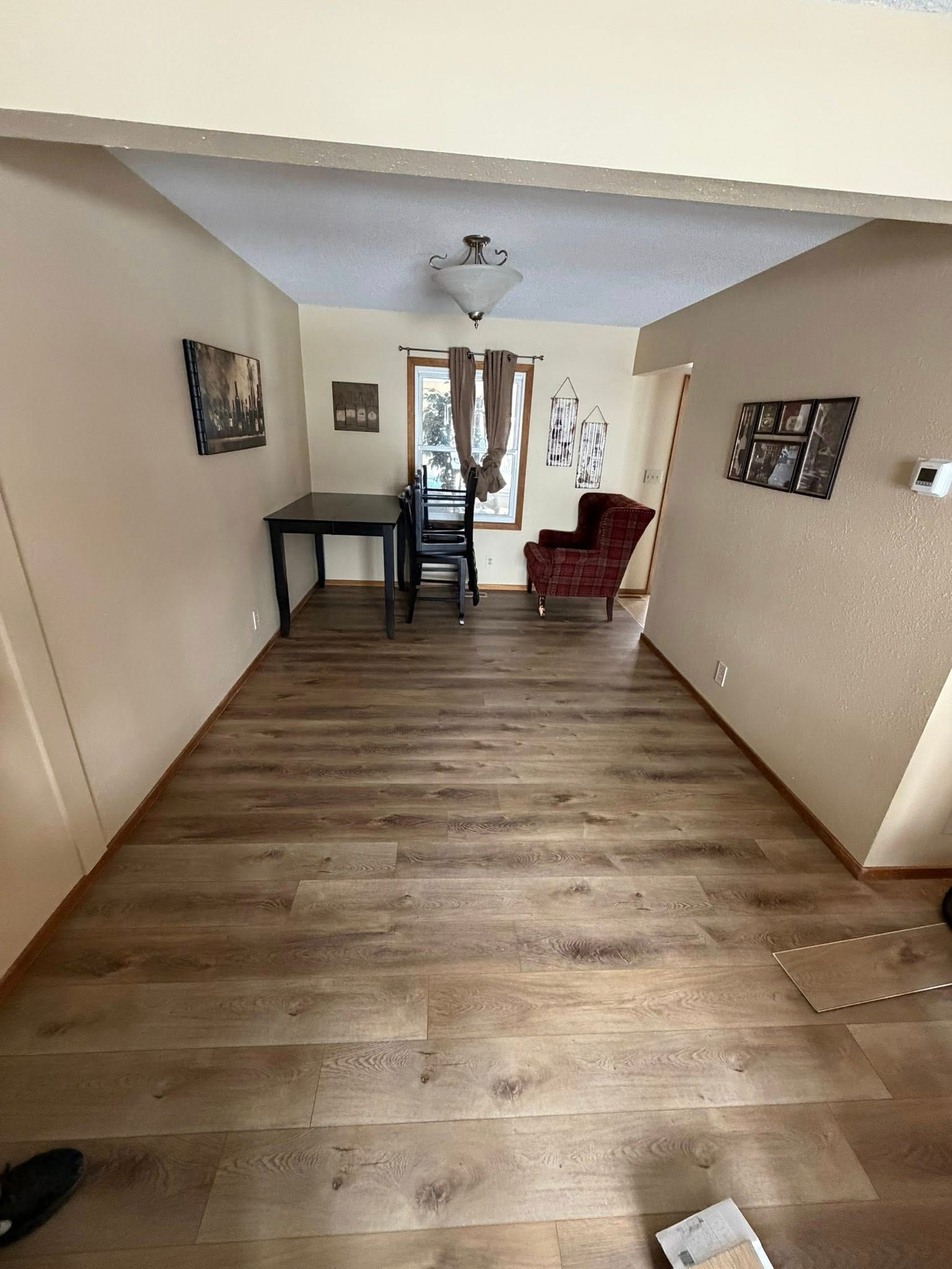 Empty living room with wood floor, white walls, small desk by a window, and a red chair near the back.