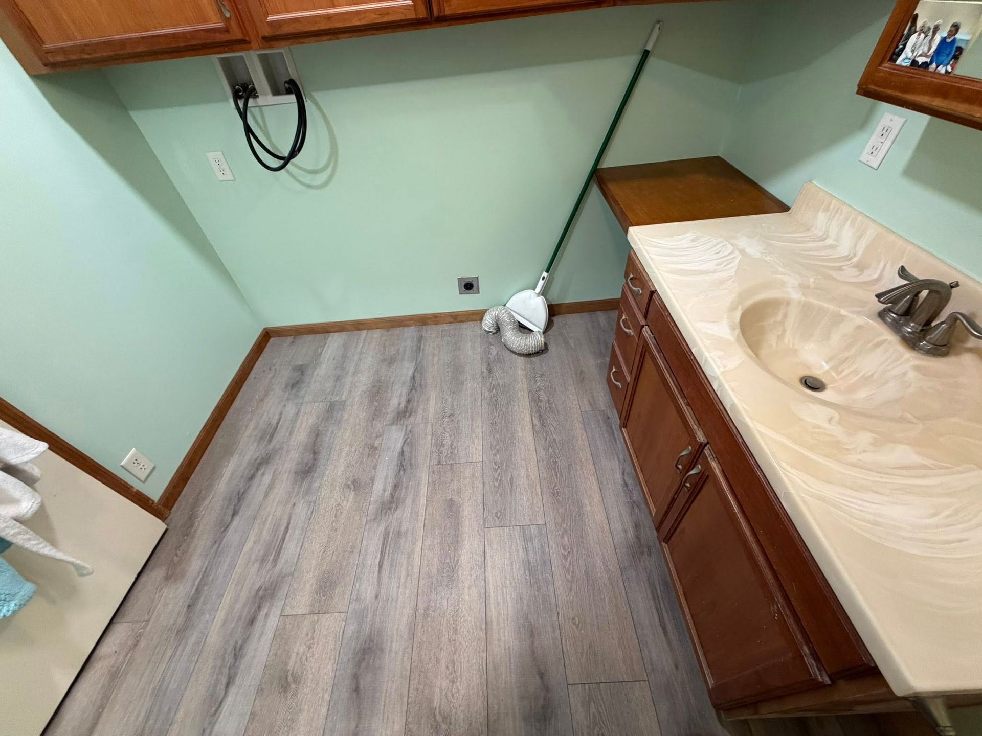 Empty kitchen with mint green walls, wood cabinets, beige countertop, and gray wood-look flooring.