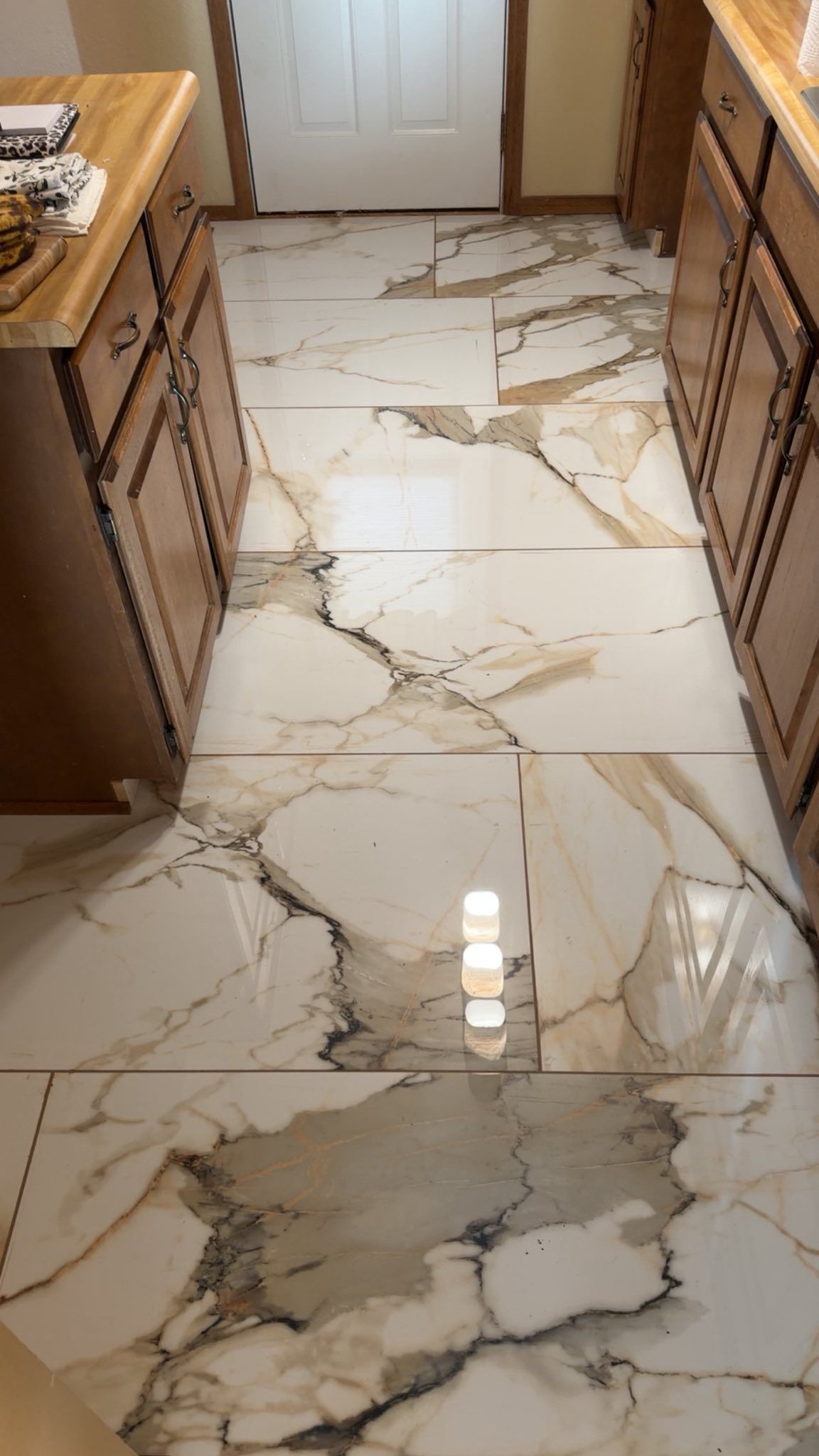 Kitchen with large white marble-look tile floor and wood cabinets on both sides