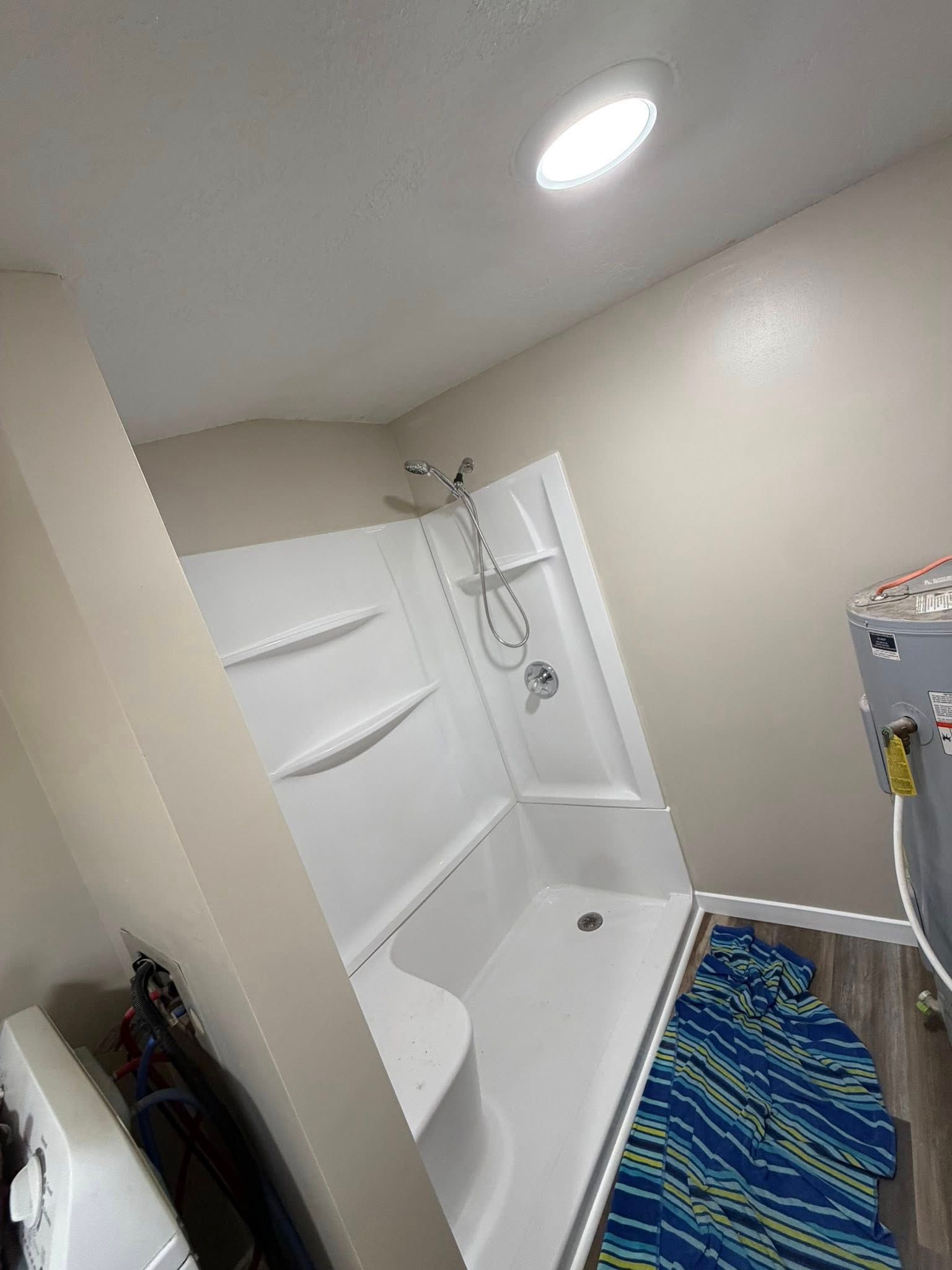 Small bathroom with a white shower-tub, built-in shelves, blue striped rug, and laundry machine.