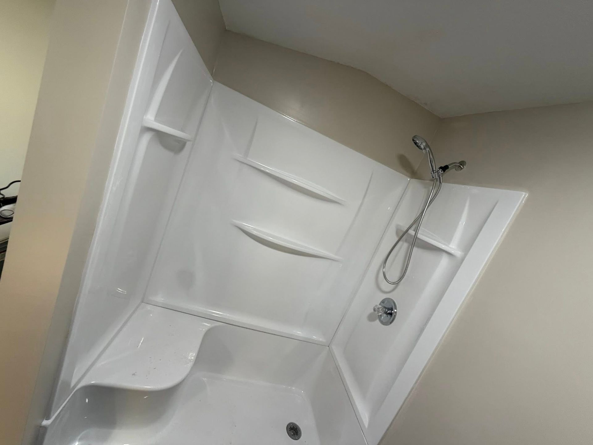 White walk-in shower with built-in seat and handheld showerhead in a beige bathroom
