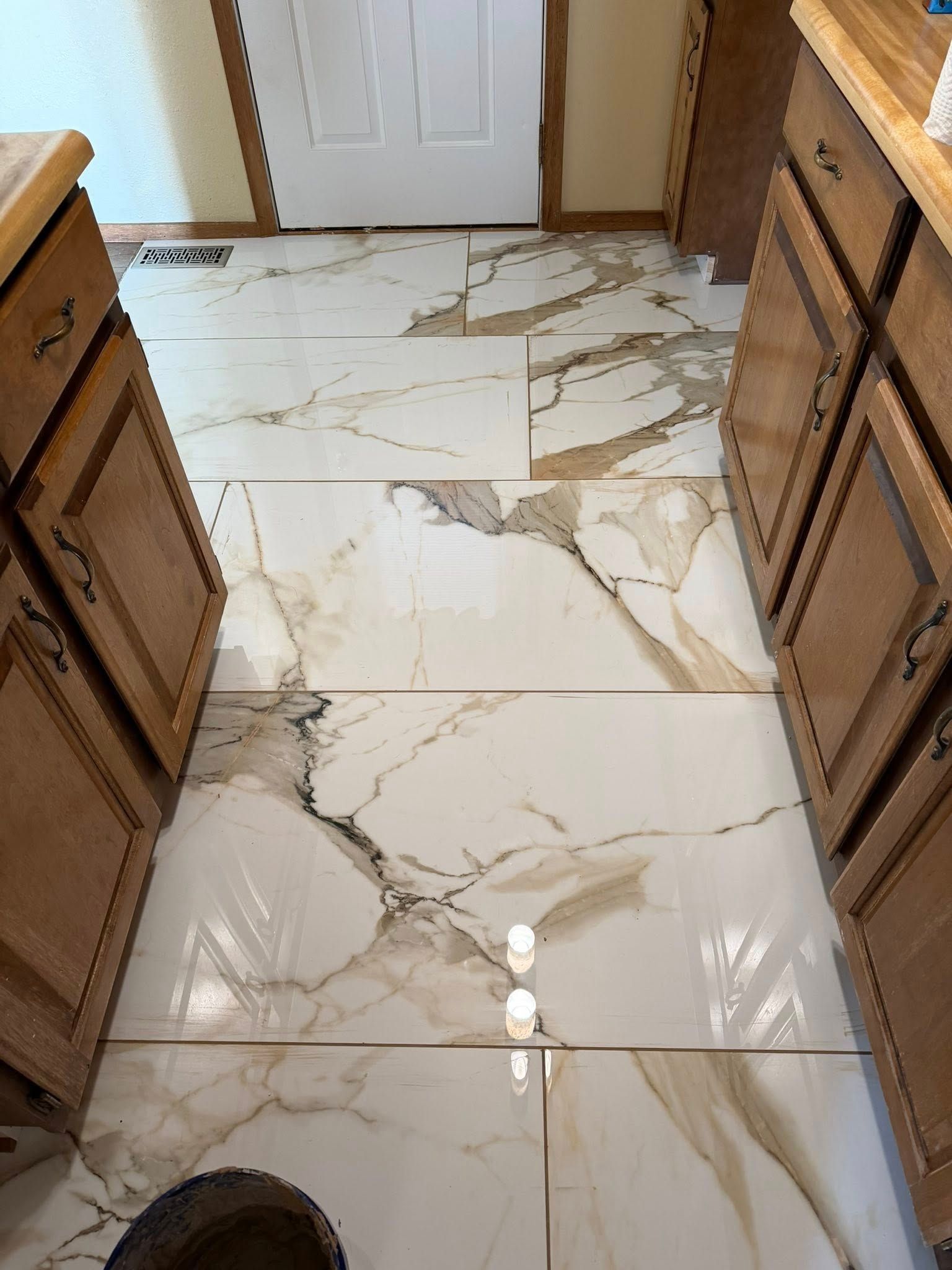Kitchen floor with glossy white marble-look tile and wooden cabinets on both sides.