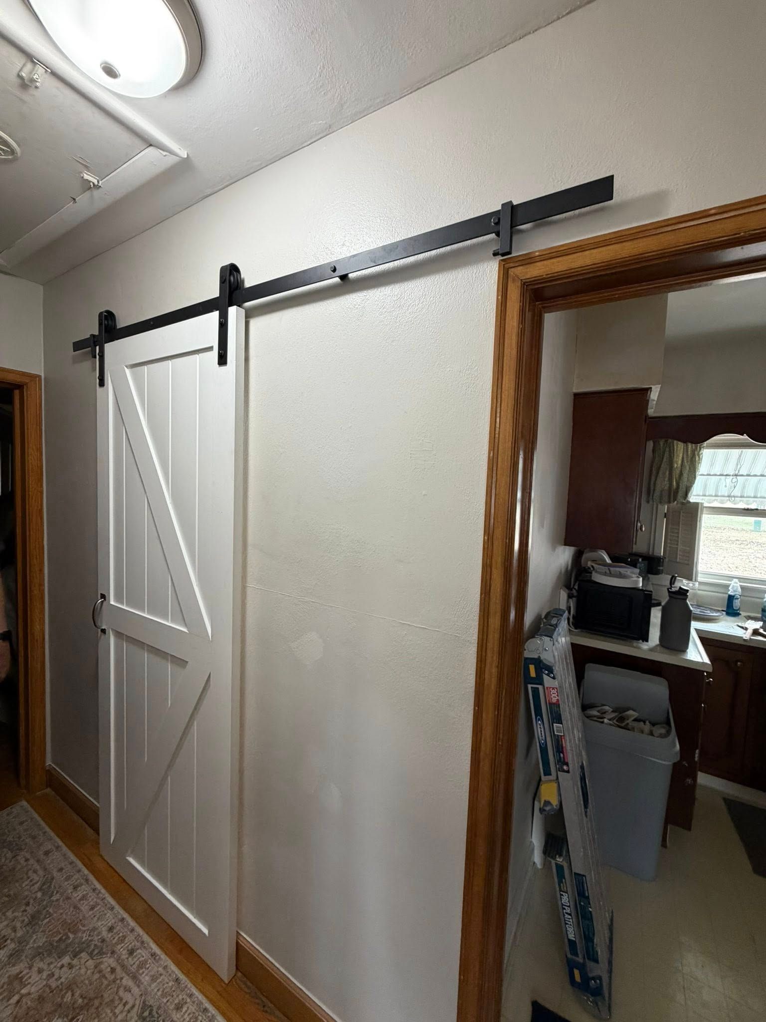 White barn door on a black track beside a hallway opening into a room