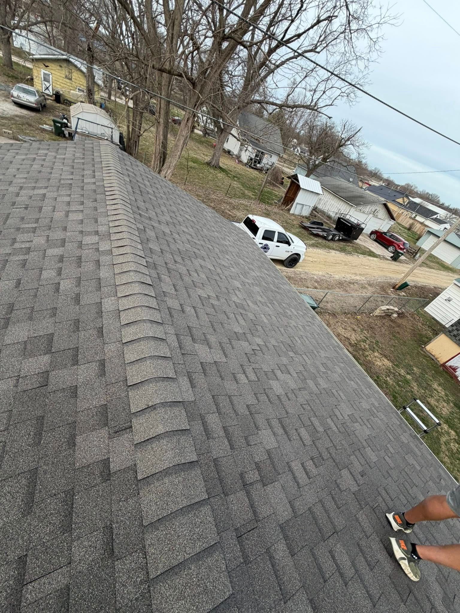 Steep gray shingled roof overlooking a yard with parked cars and leafless trees