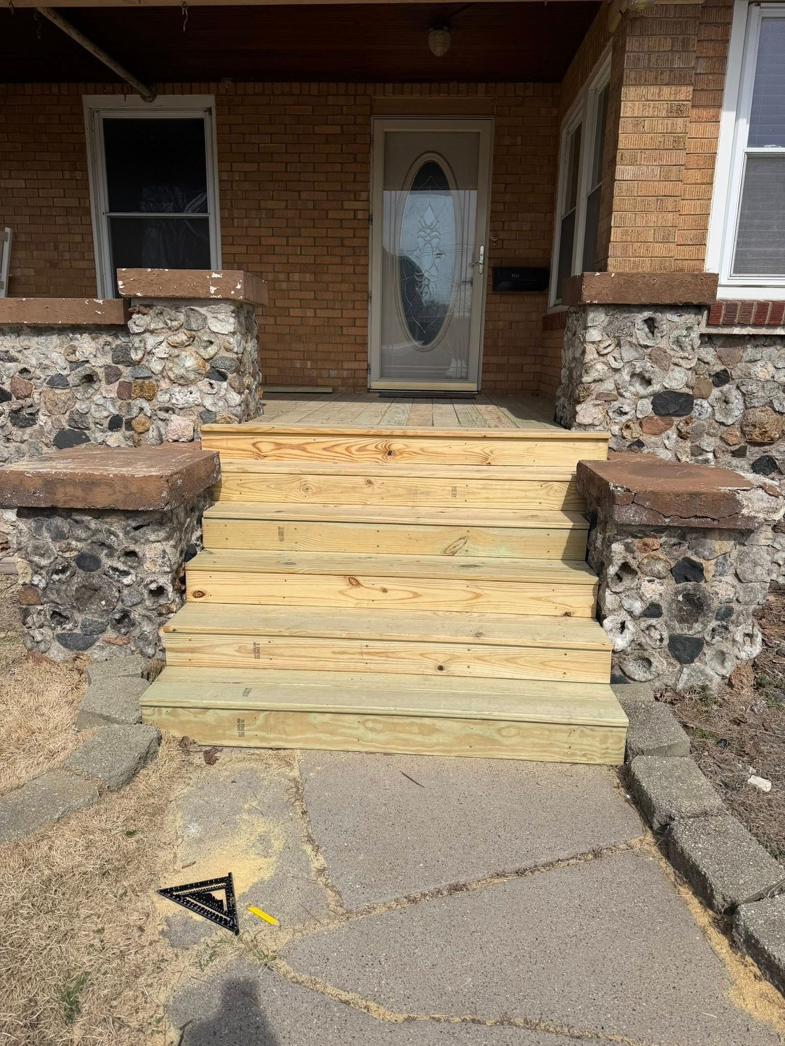 Front steps with wooden stairs leading to a brick house entrance and glass door