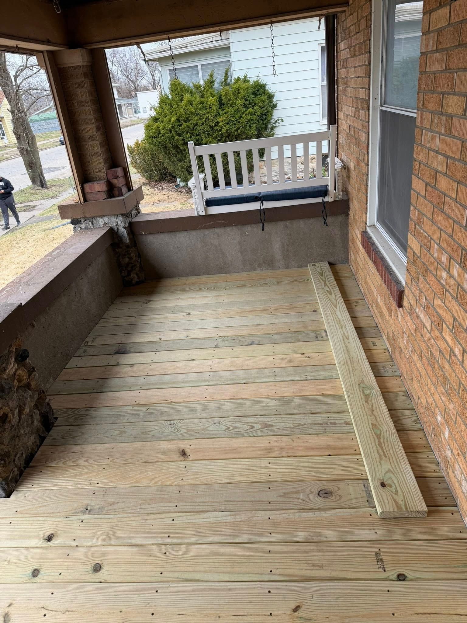 Covered brick porch with wooden ramp, bench, and railing leading to a front yard view