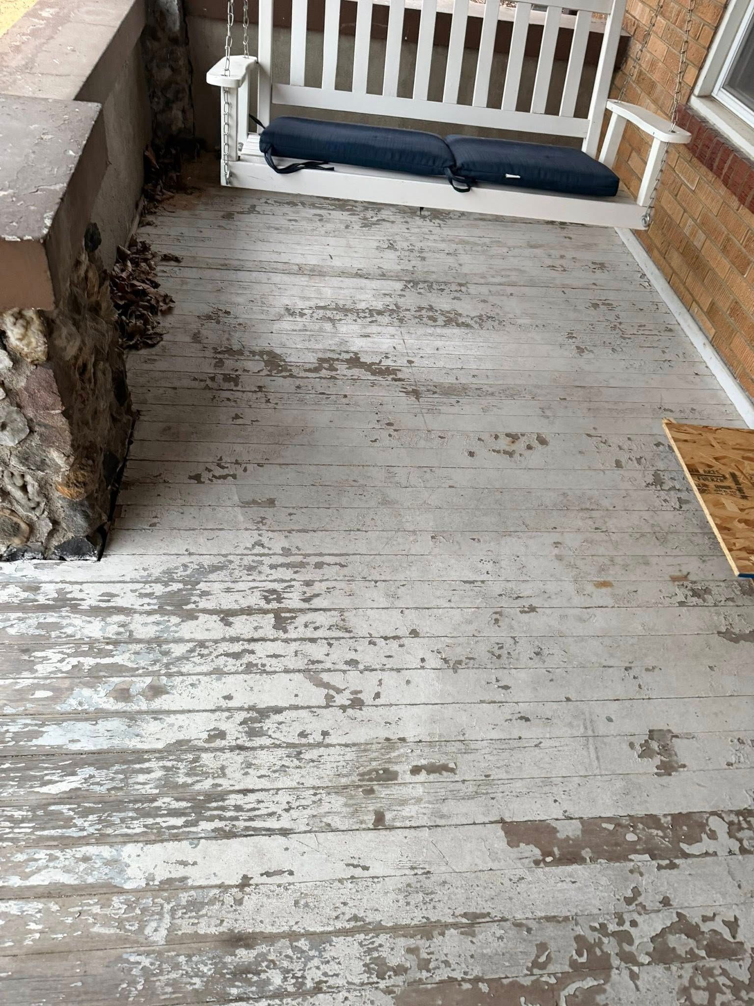 Weathered wooden porch floor with a white railing and a dark bench at the far end