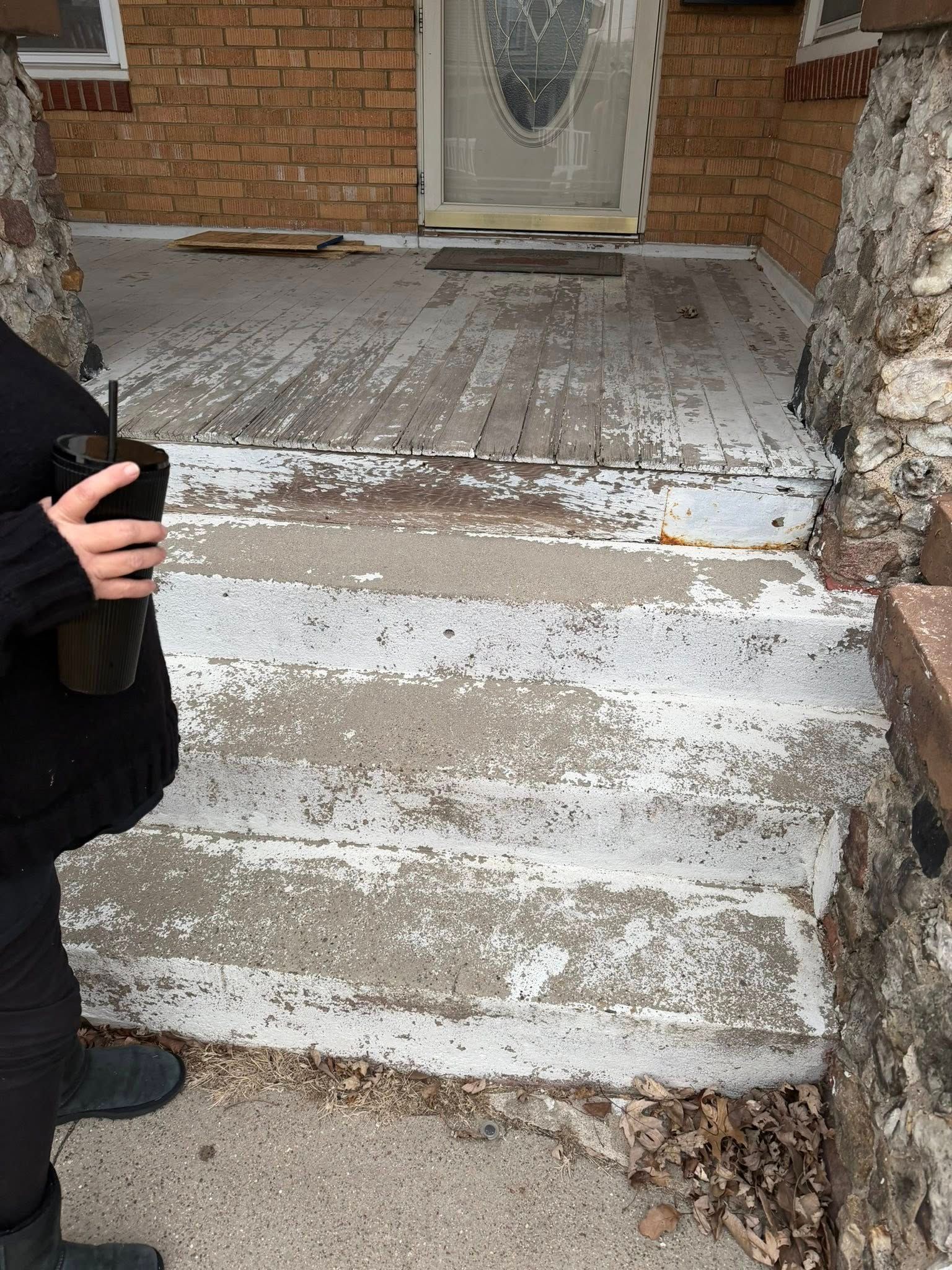 Chipped white front steps leading to a brick house entrance, with a person standing at left.