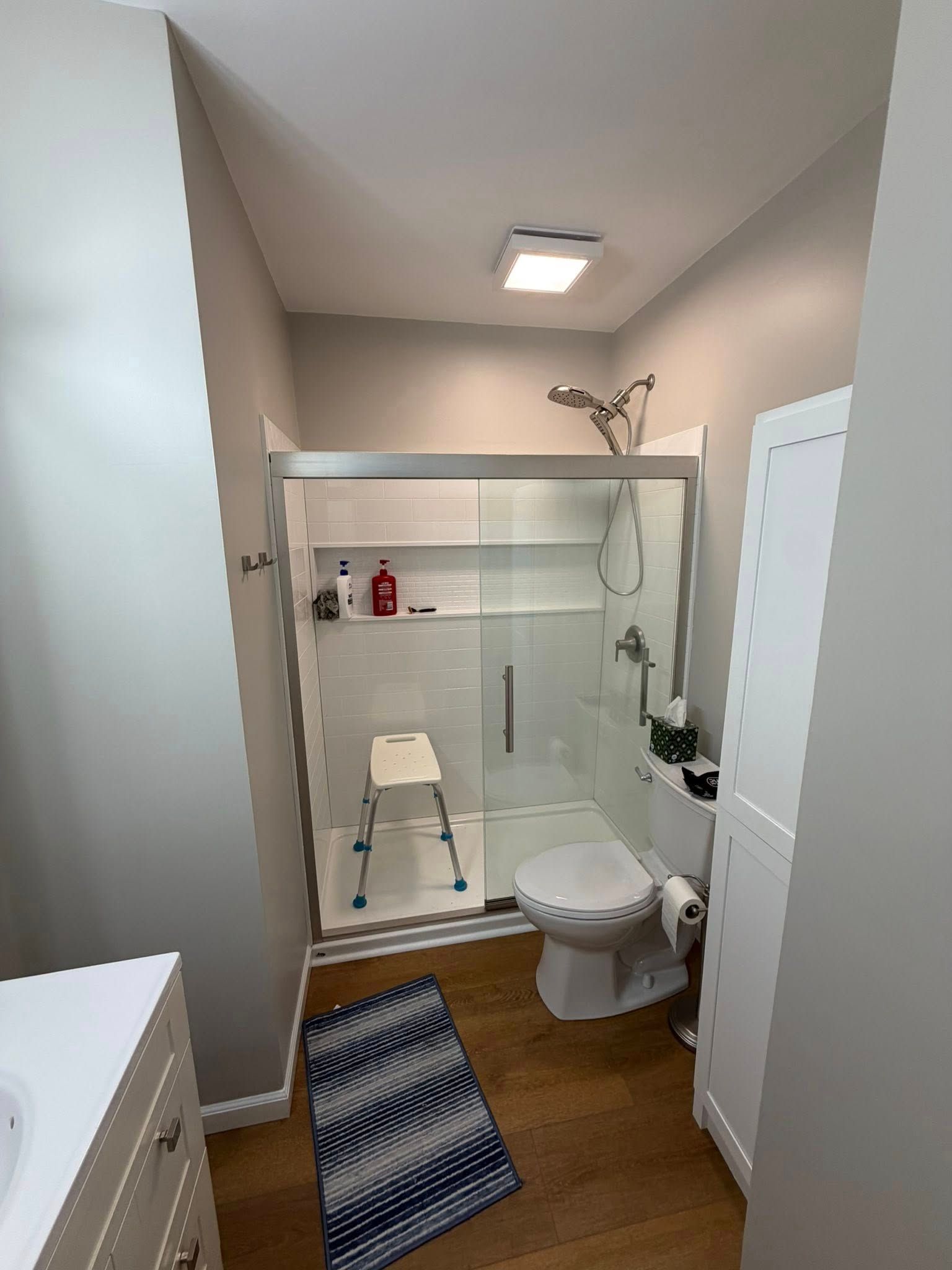 Small bathroom with shower, toilet, sink, white cabinetry, and blue striped rug.