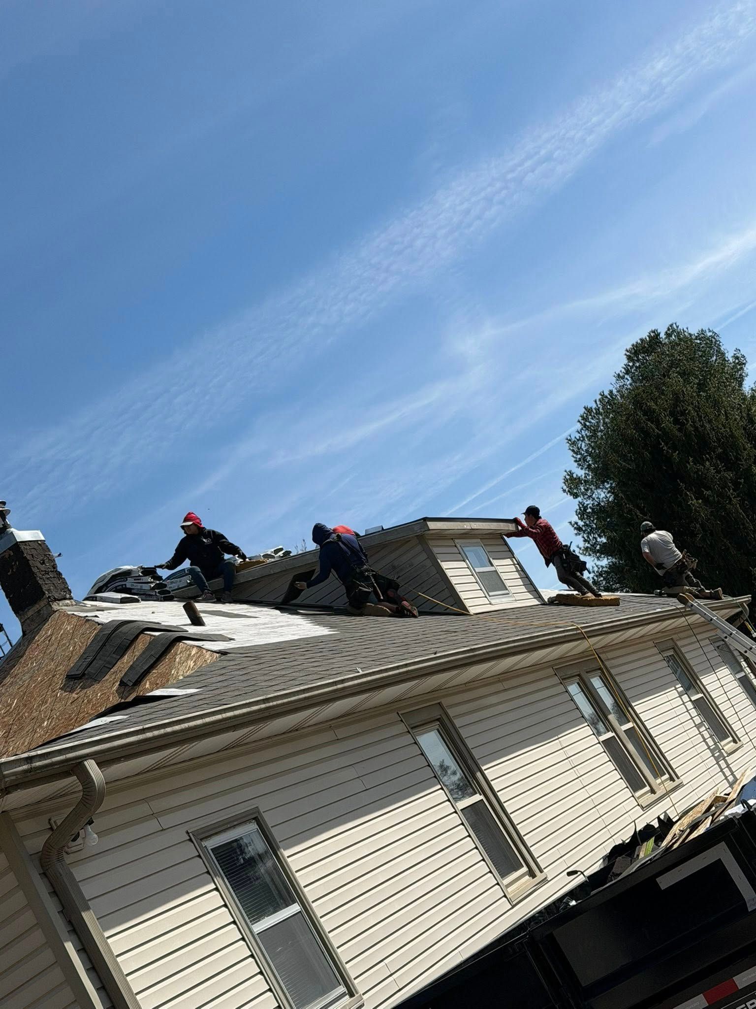 Workers repairing a house roof under a clear blue sky