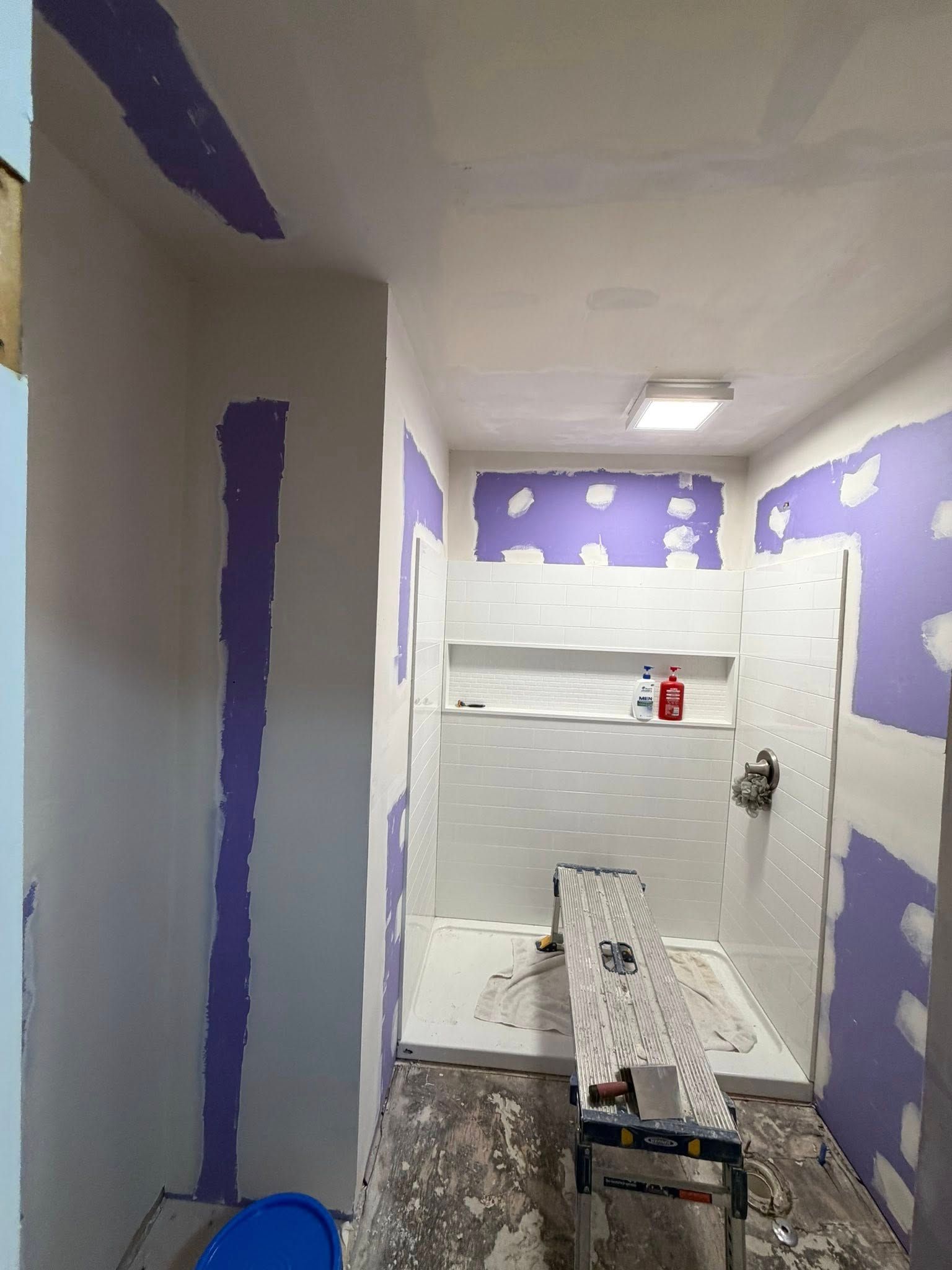 Small bathroom under renovation with purple drywall patches, a shower, and a sink in the foreground