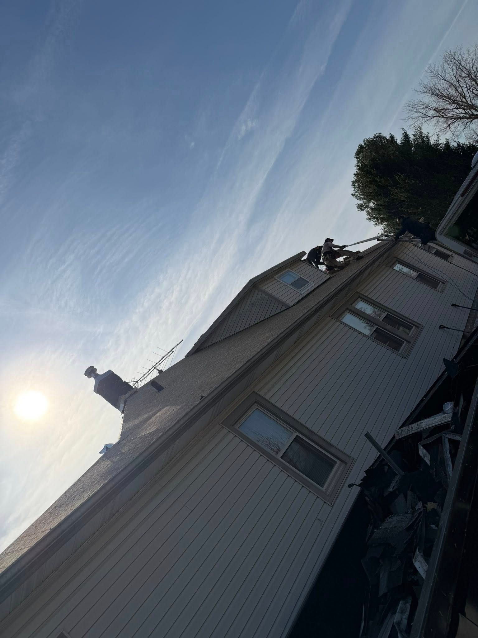 Sunlit white house viewed at an angle, with blue sky, trees, and rooftop silhouettes above