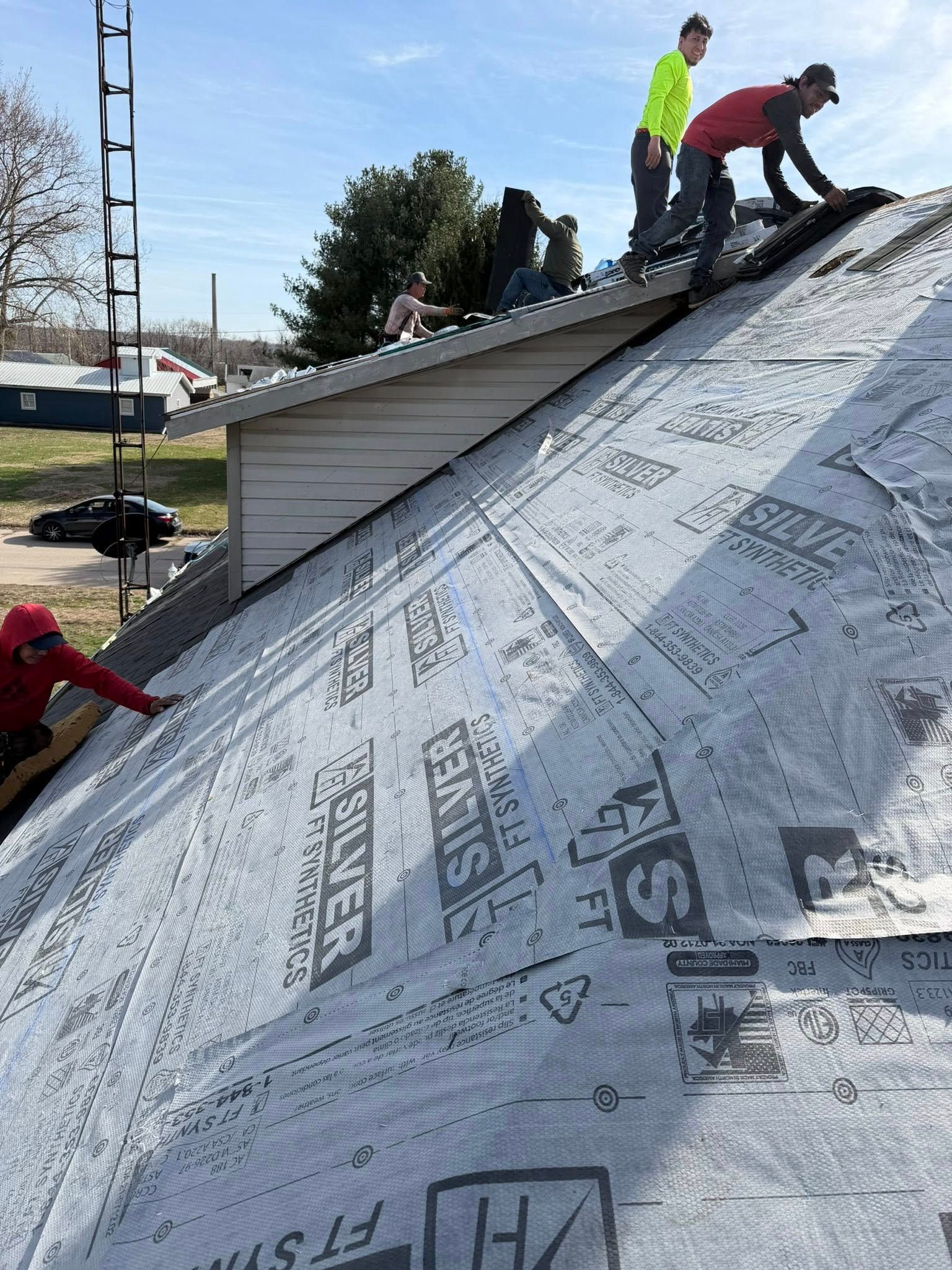 Workers installing roofing underlayment on a steep roof, with one person crouched near the ridge.