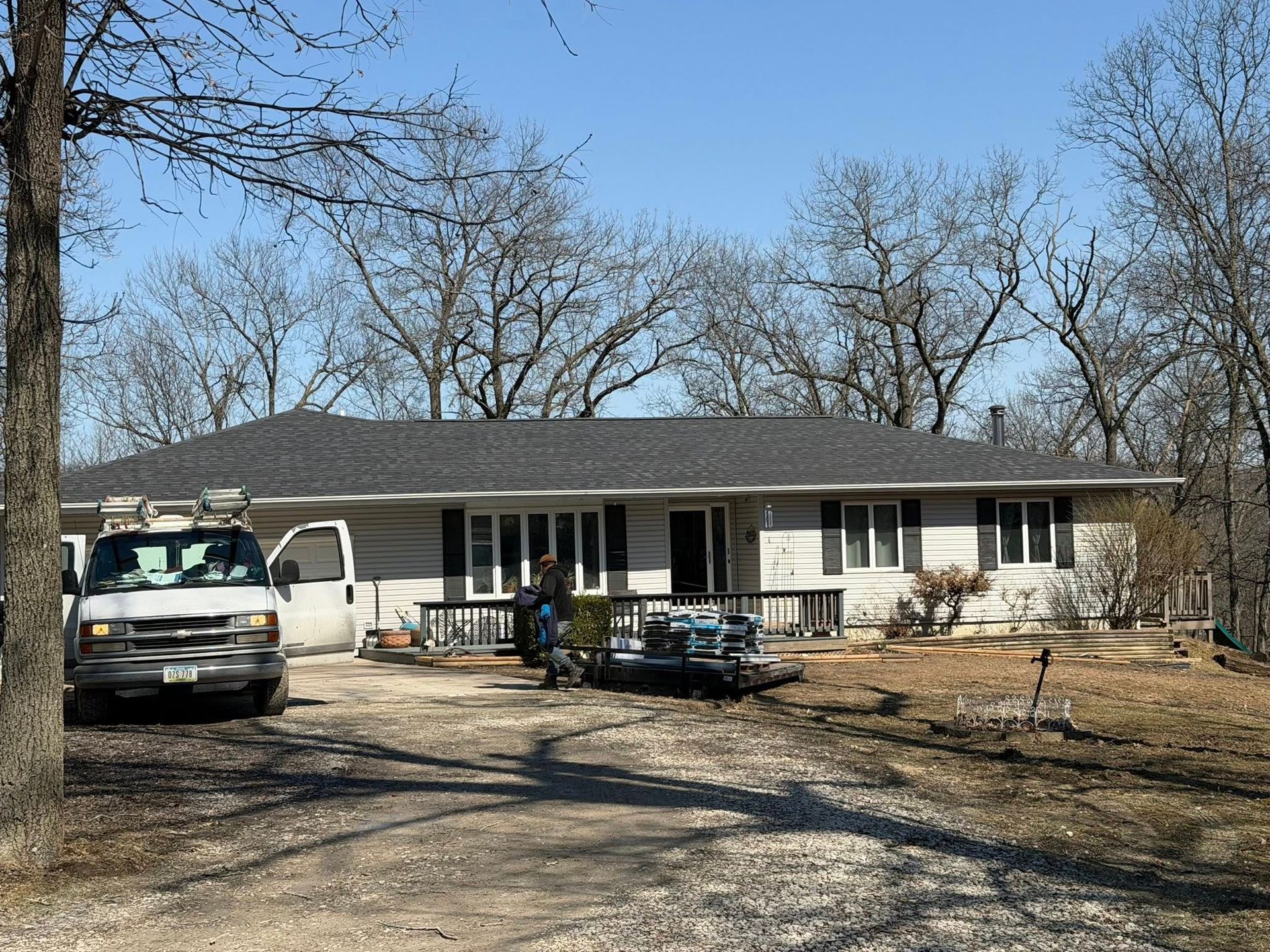 Single-story house with parked vehicles and bare trees in a rural yard on a clear day