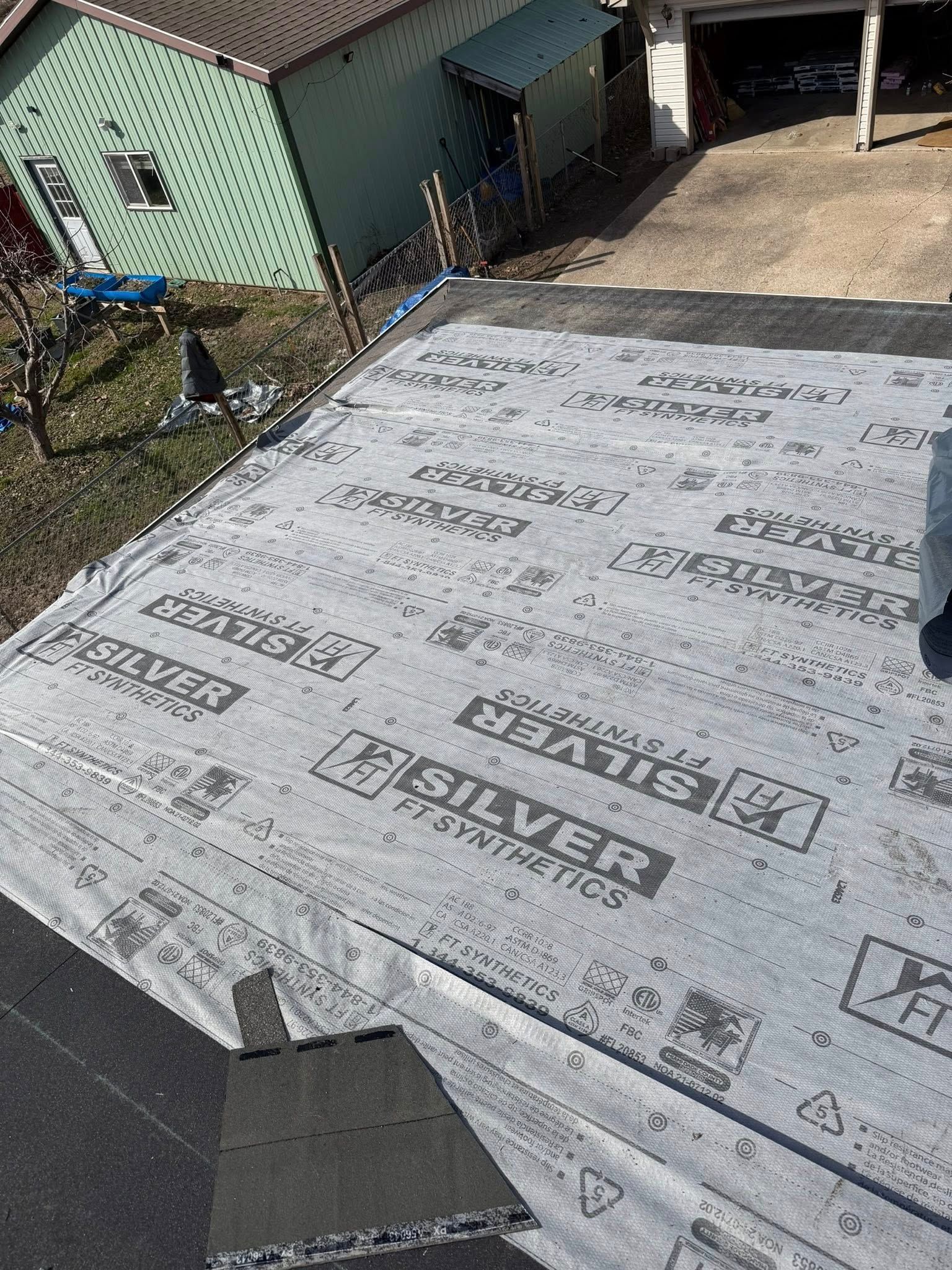 Roof under construction with gray underlayment, adjacent house, and driveway in the background
