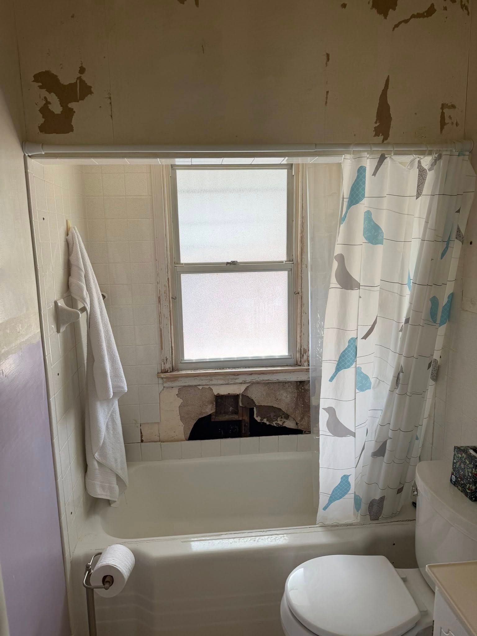 Small bathroom with a worn tub, blue shower curtain, towel rack, and frosted window above the sink.