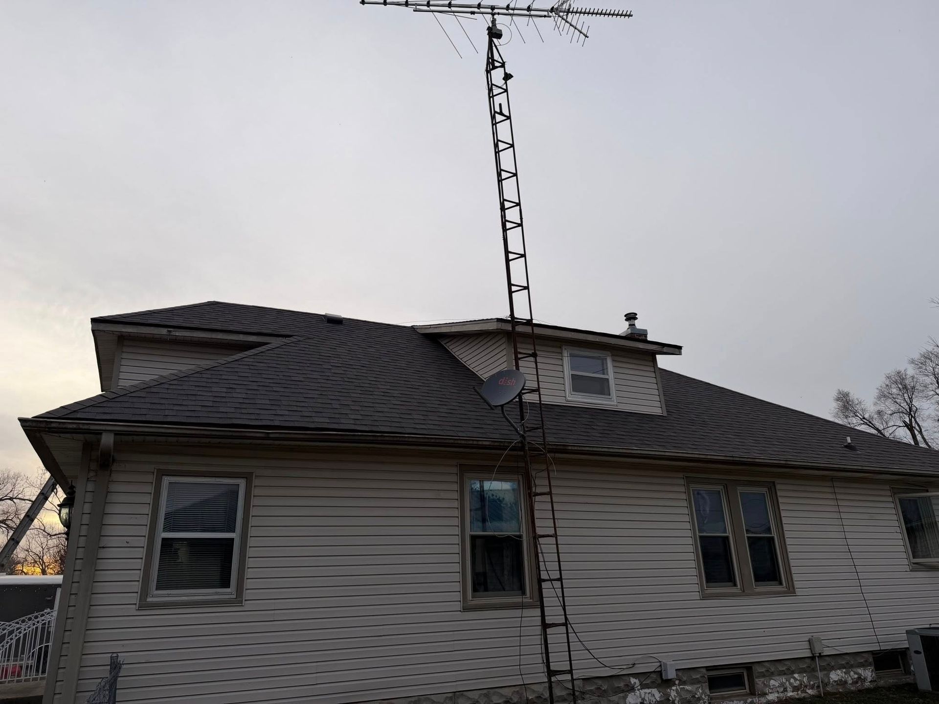 House with damaged roof and tall antenna at dusk