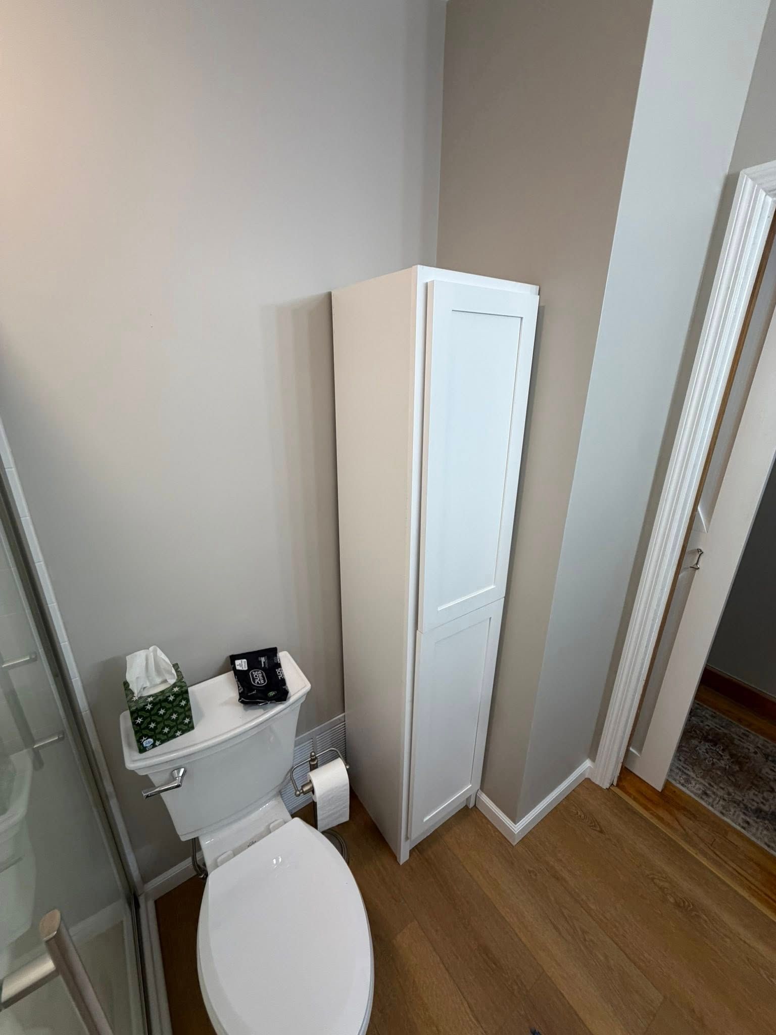 Small bathroom with toilet, white storage cabinet, and wall mirror beside a gray wall and wood floor.