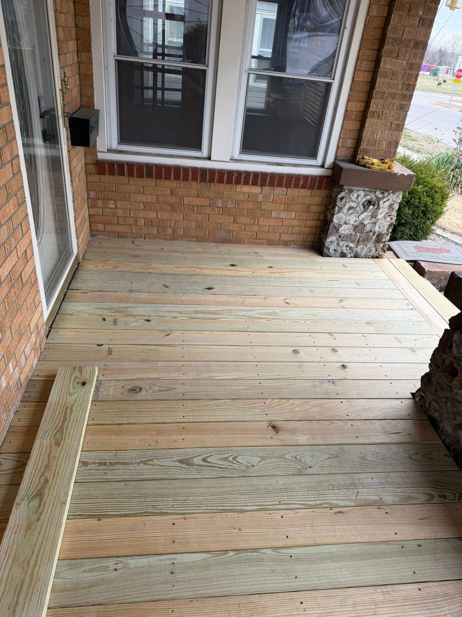 Wooden porch ramp leading to a brick house entrance with windows and steps.