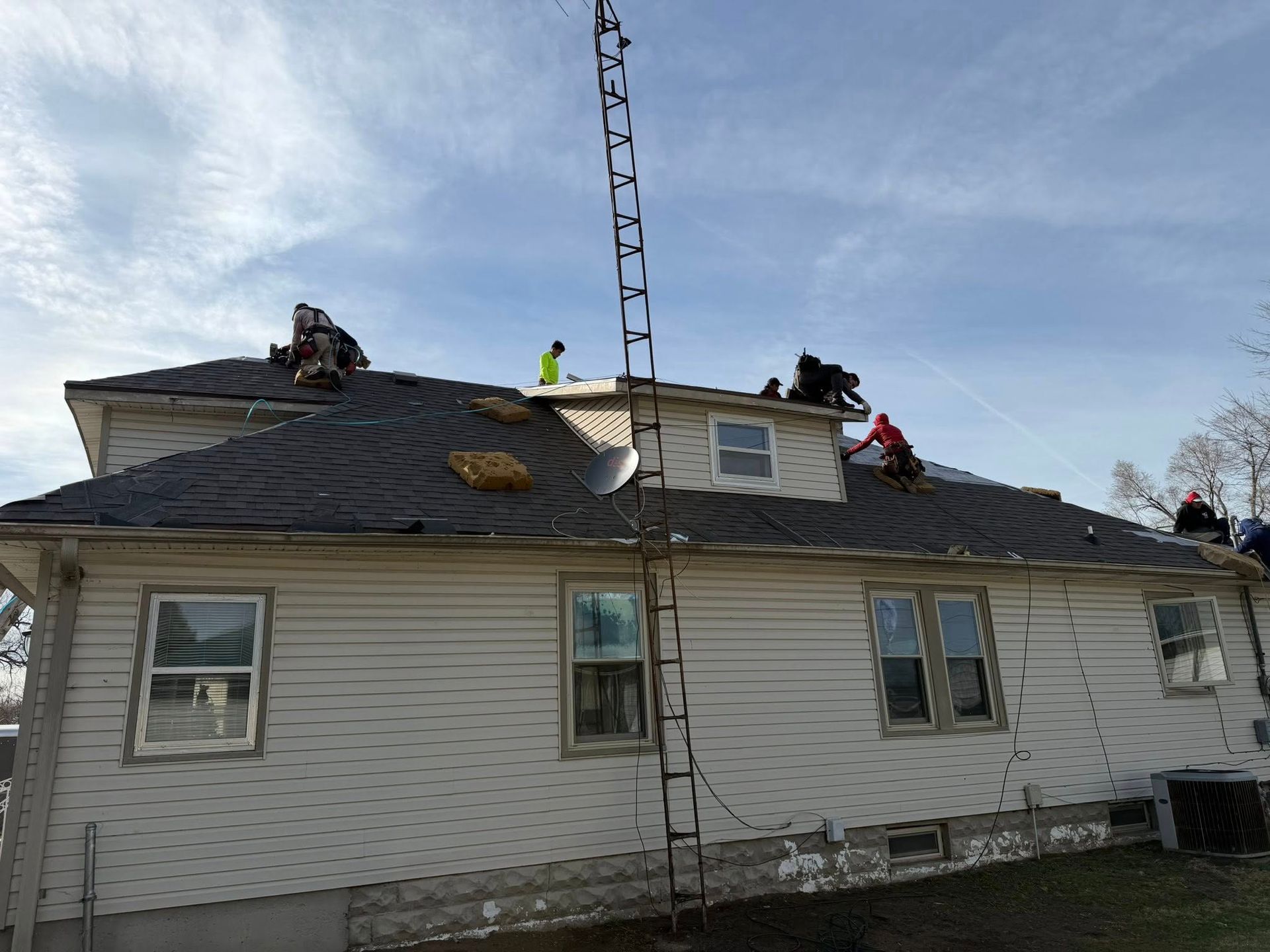 Workers repairing a roof on a white house with a ladder under a blue sky