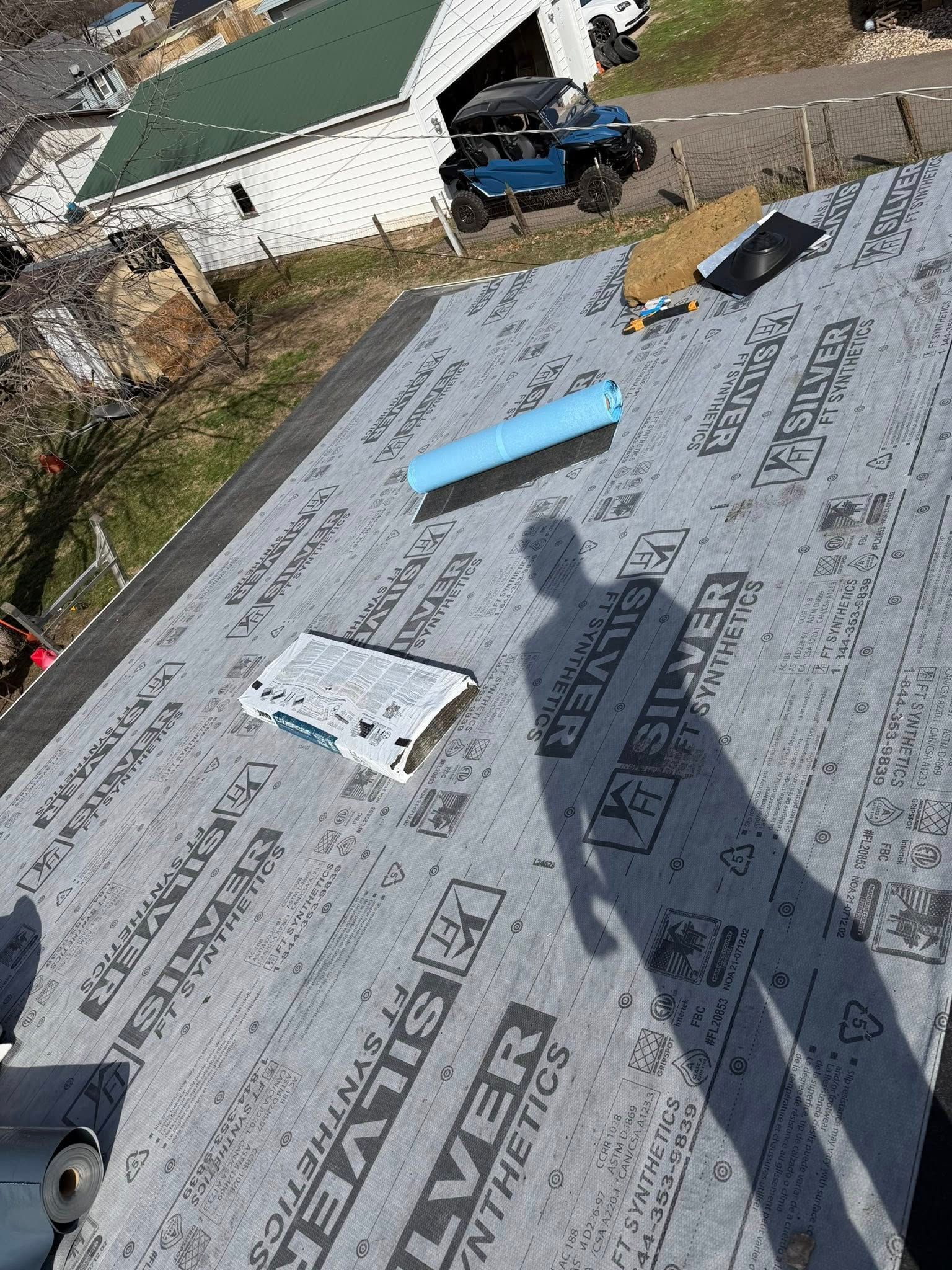 Roof under construction with black roofing paper, blue foam insulation, and tools on a sloped surface.