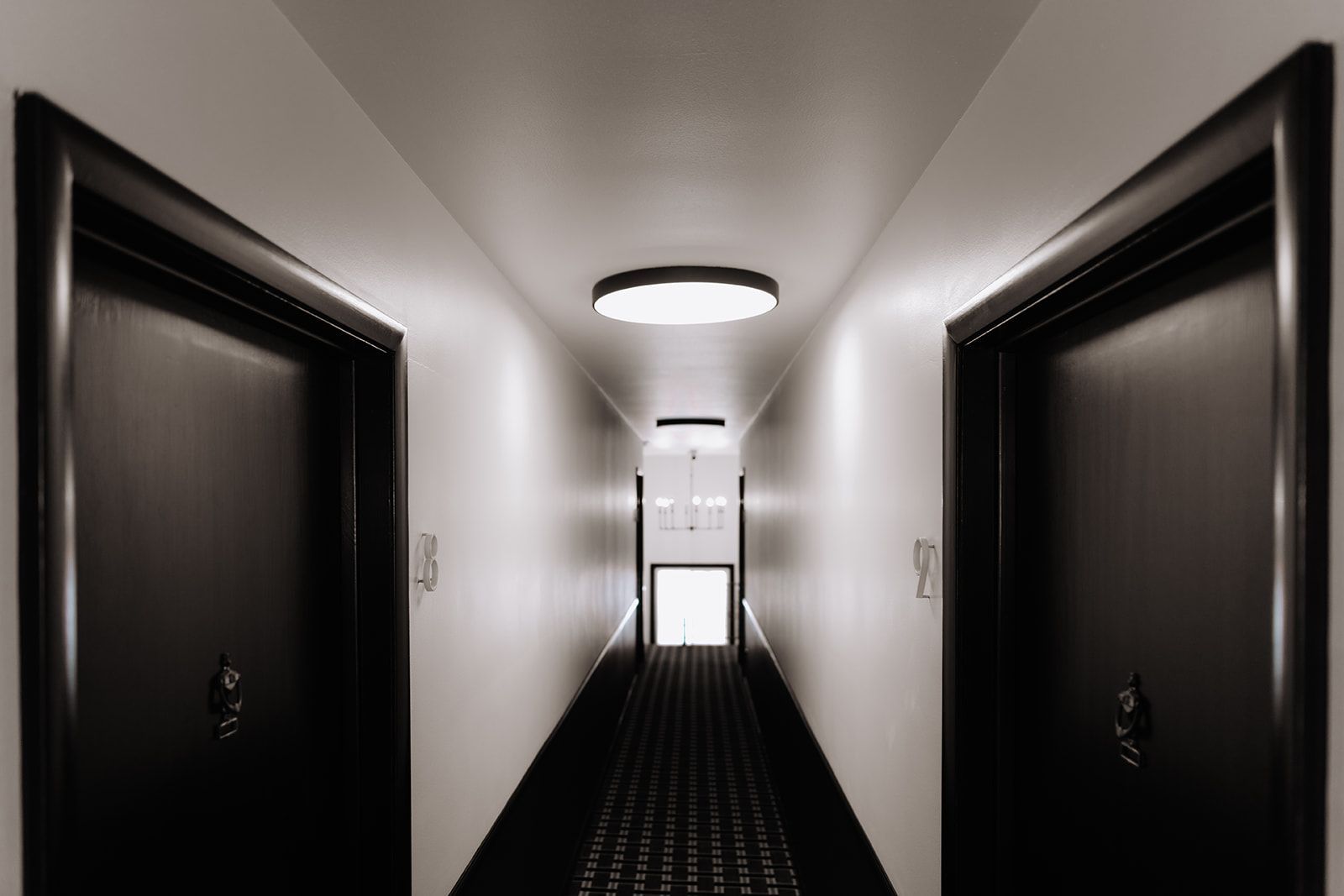 Semi-modern looking apartment hallway with reflective lighting effects. Black doors in a white hallway. The ceiling lights are big and circular and modern. South Minneapolis apartments by RightMove Properties.
